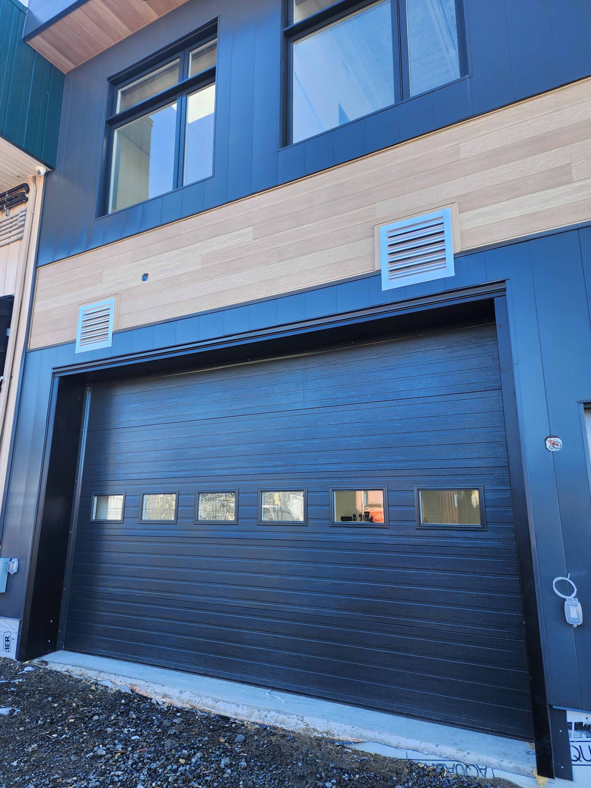 Bâtiment moderne avec une porte de garage foncée, un revêtement en bois clair et un extérieur bleu foncé.