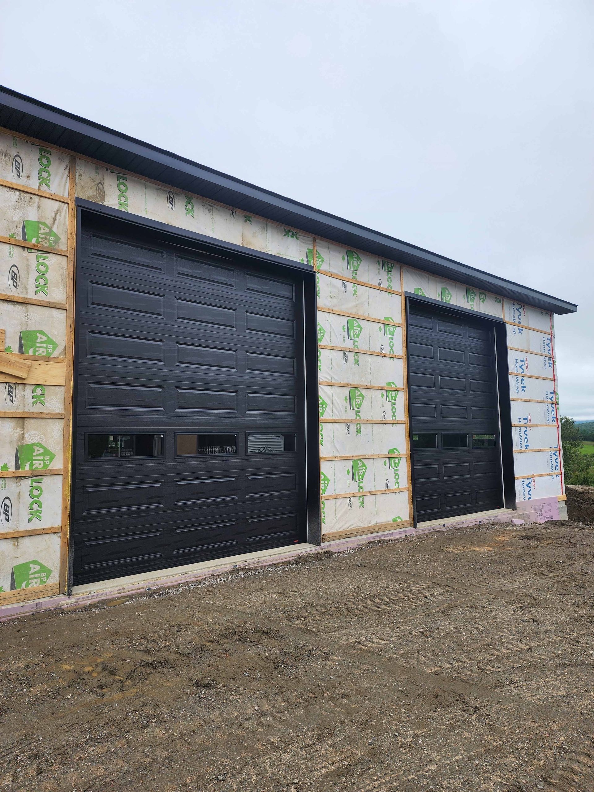 Trois portes de garage noires sont placées l'une à côté de l'autre sur le côté d'un bâtiment.