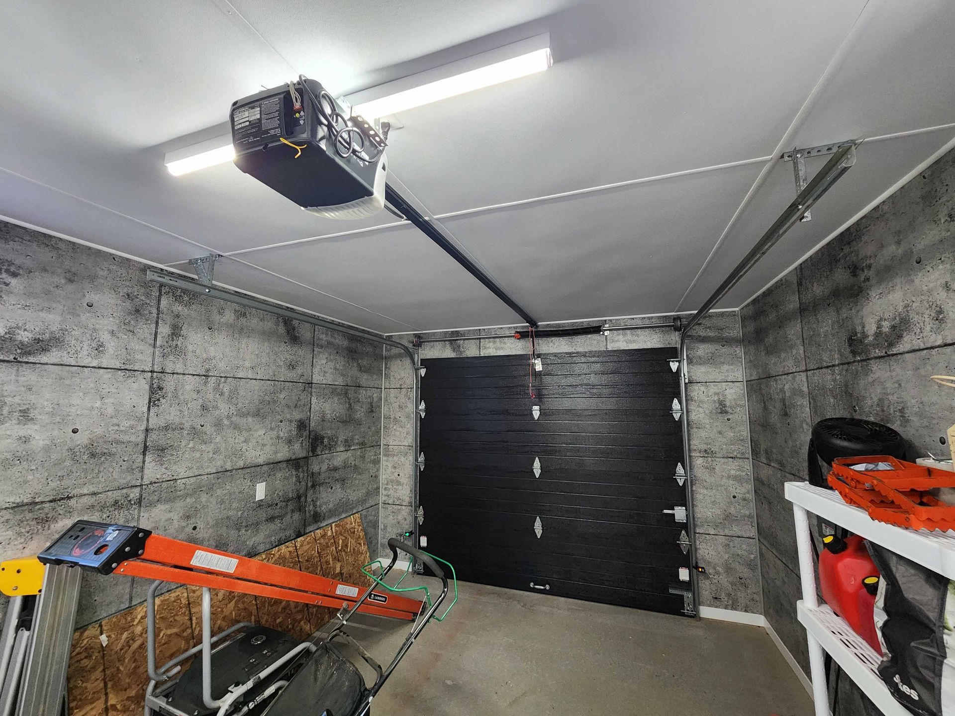 Un garage avec une porte de garage ouverte et une échelle suspendue au plafond.