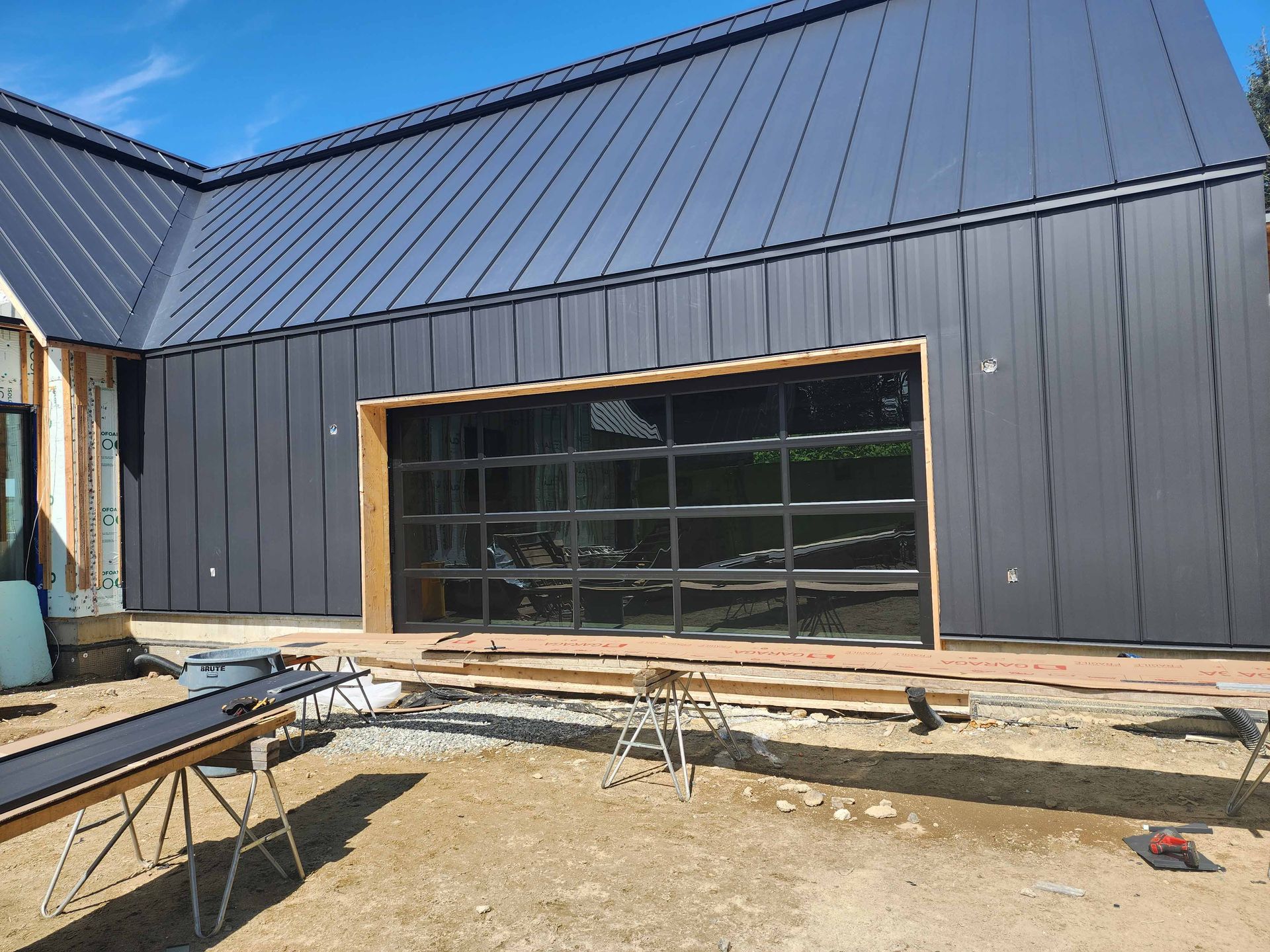 Bâtiment revêtu de métal noir avec une grande porte de garage vitrée en construction ; finitions en bois clair.