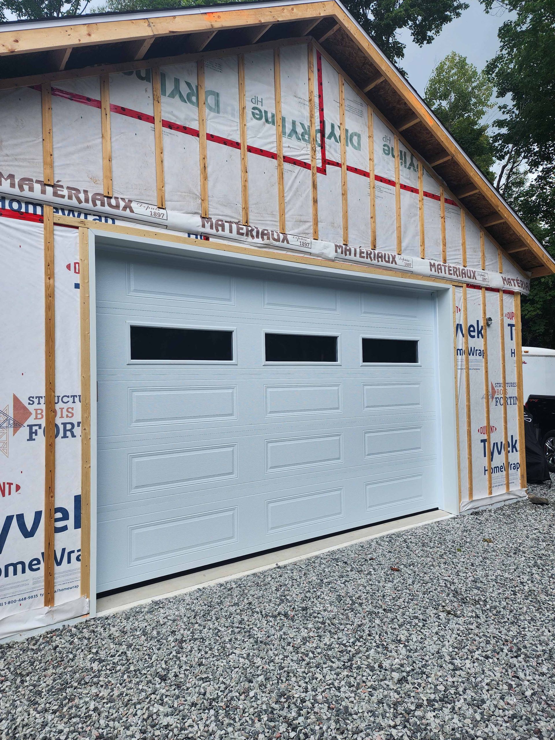 Une porte de garage blanche est en cours d'installation sur le côté d'un bâtiment.