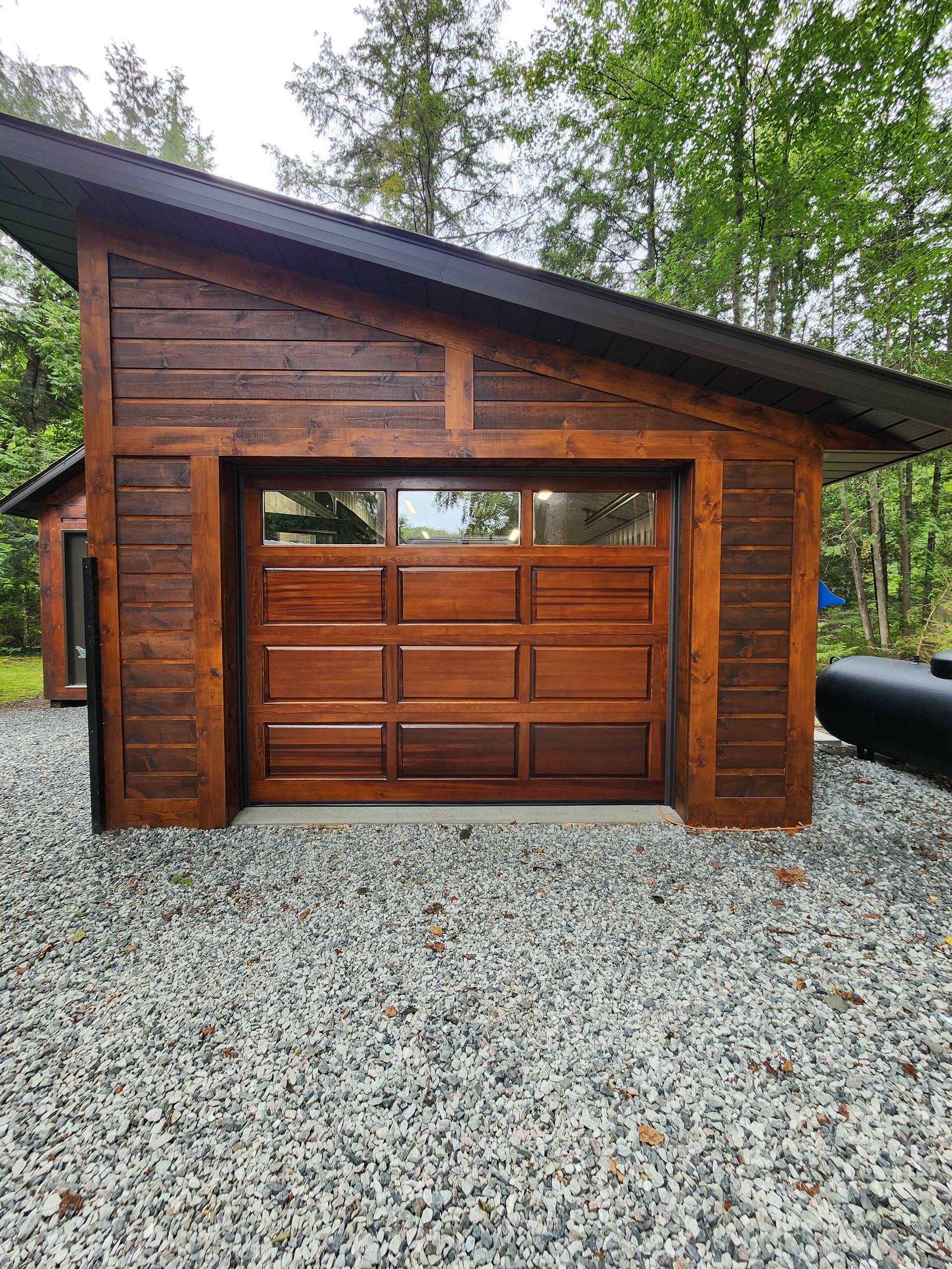 Un garage en bois avec une porte en bois et une allée en gravier.