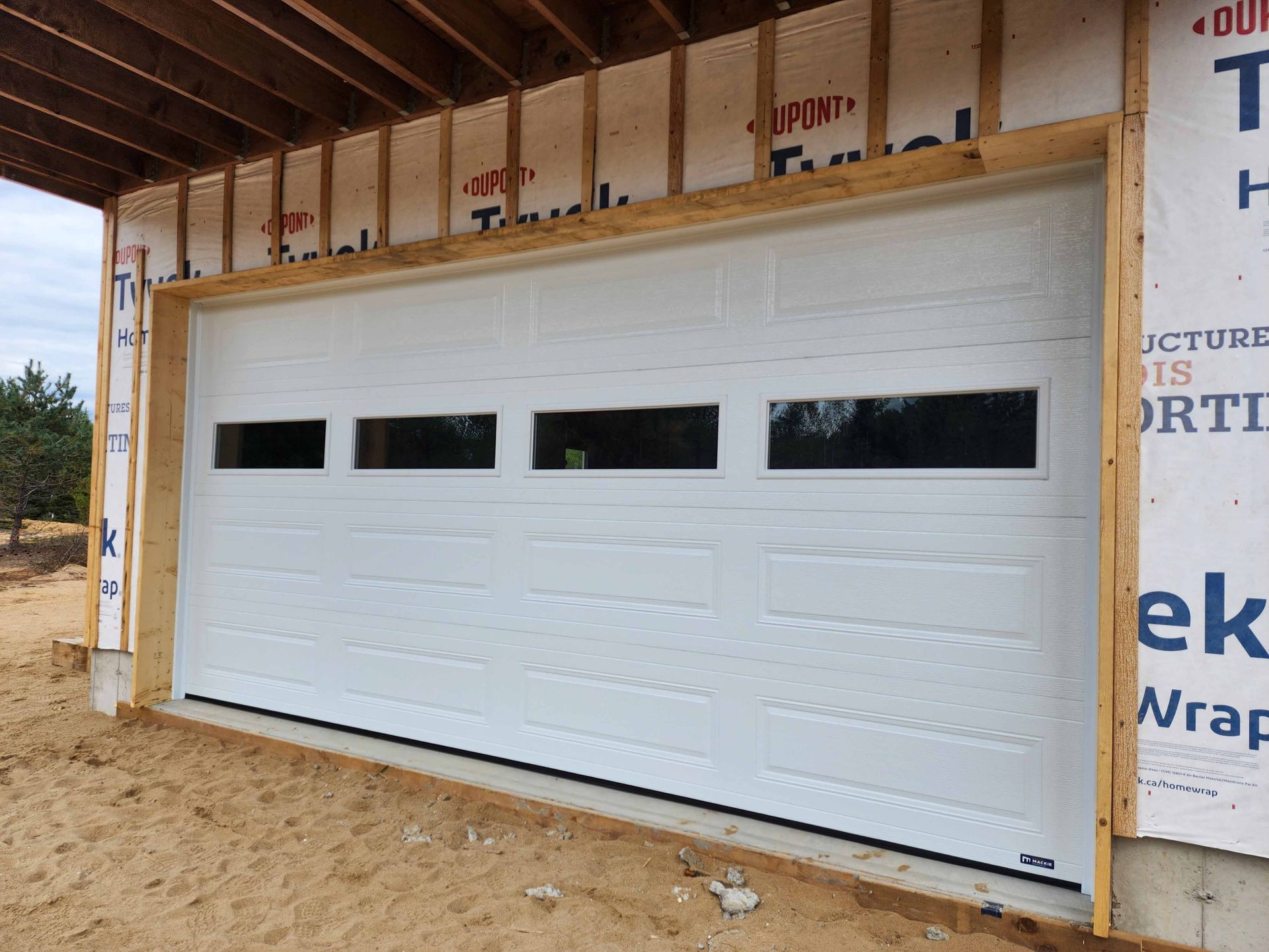 Une porte de garage blanche est en cours d'installation sur le côté d'un bâtiment en construction.