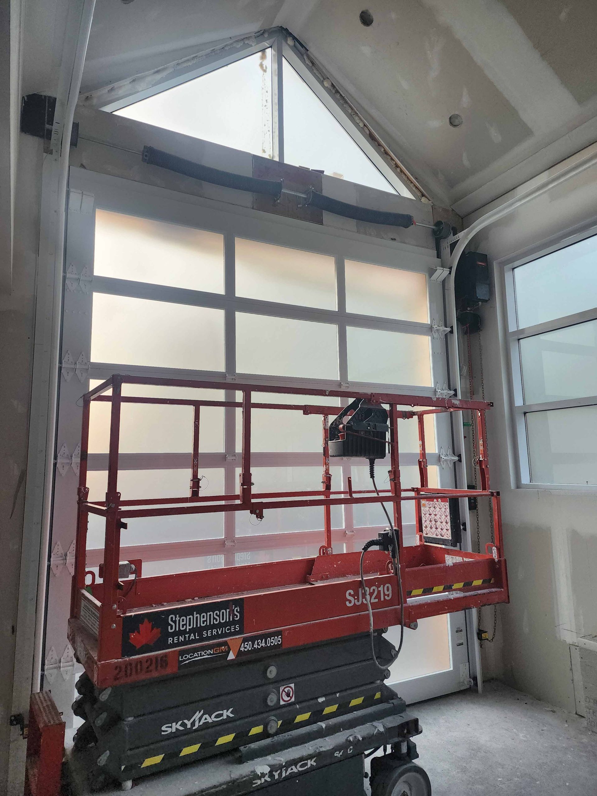 Une plateforme élévatrice devant une porte de garage en verre dépoli avec une fenêtre triangulaire en partie supérieure.