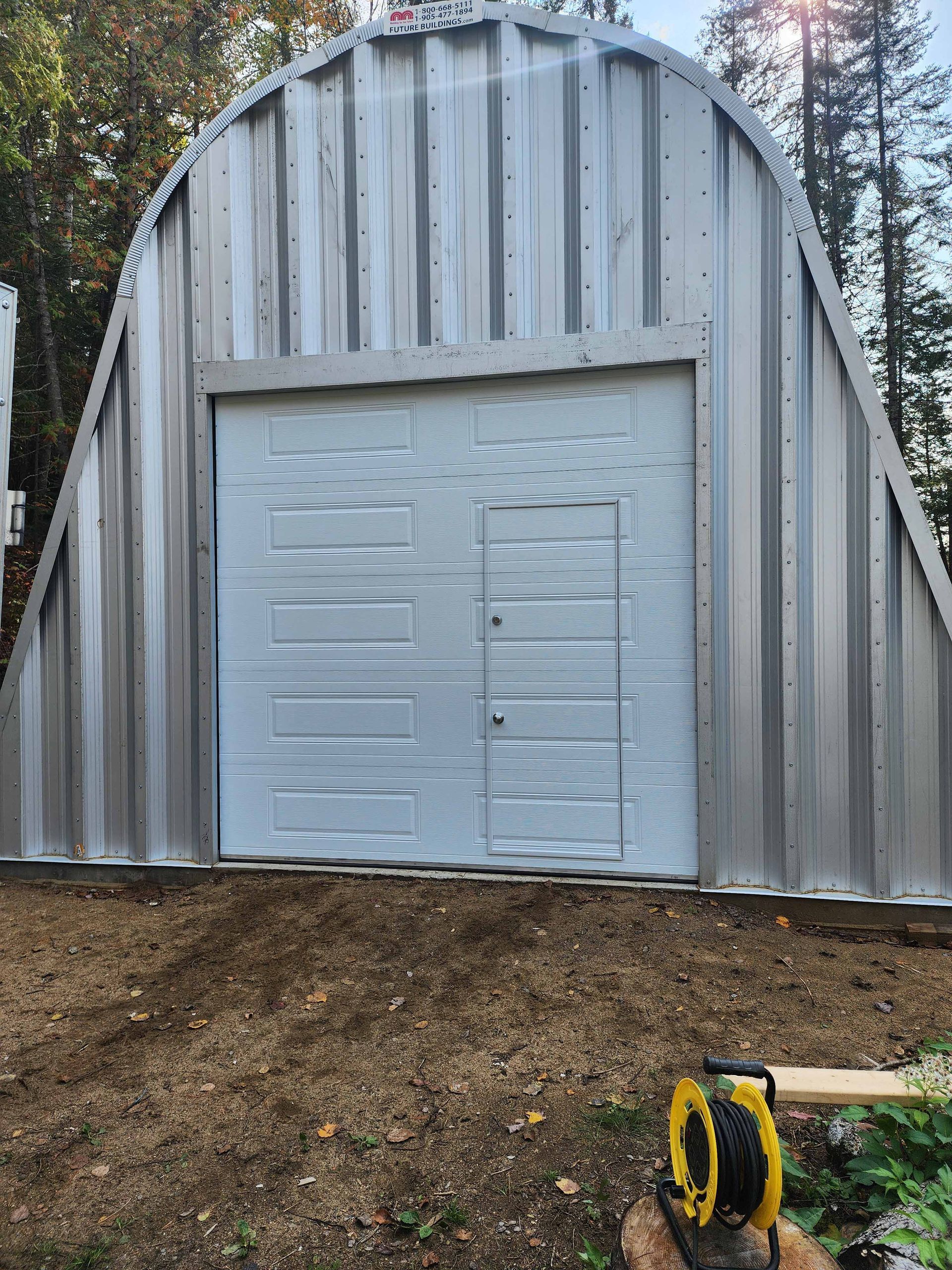 Un garage en métal avec une porte blanche est situé au sommet d'une colline de terre.