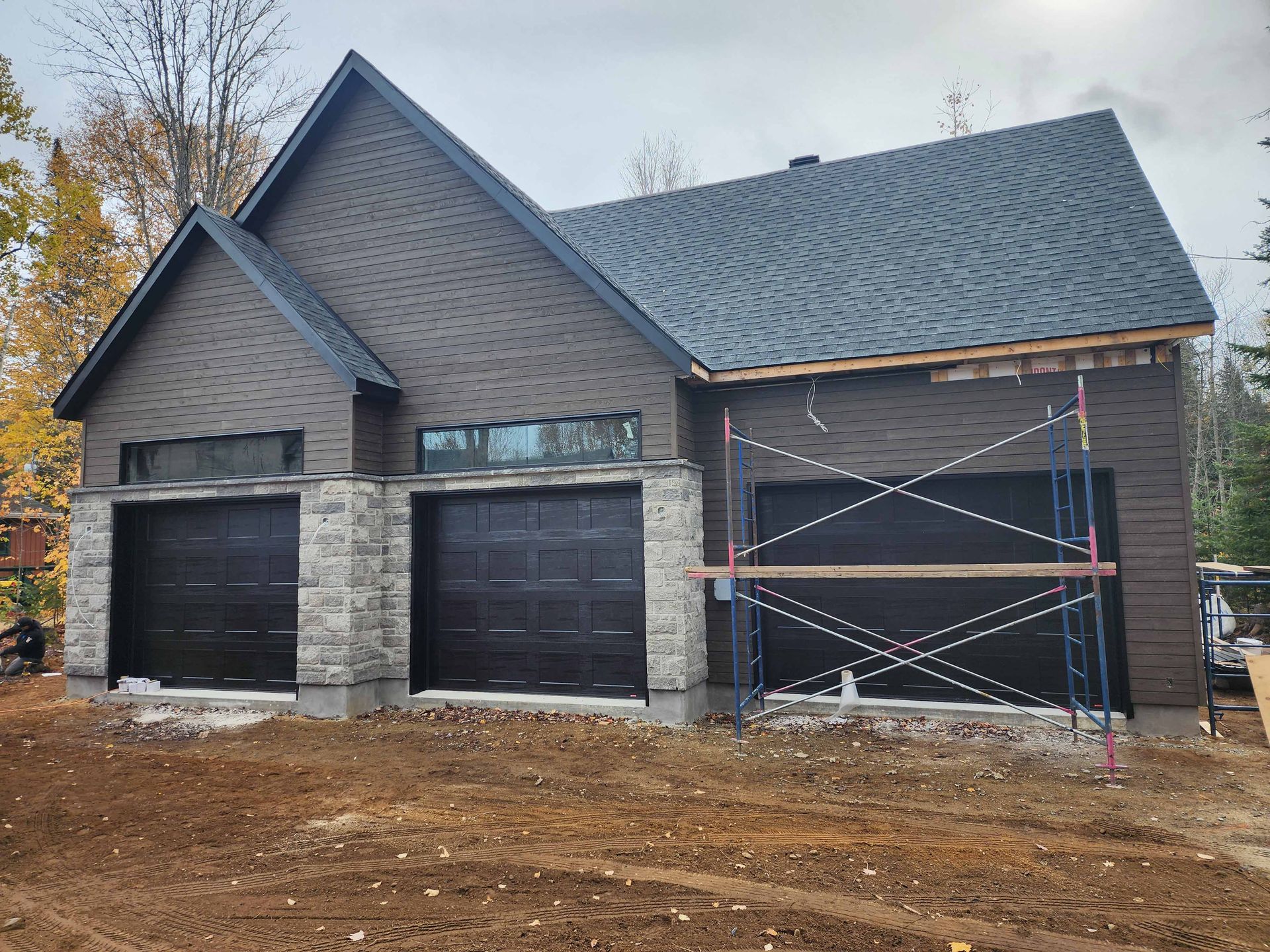 Une maison en construction avec deux portes de garage et un échafaudage devant.