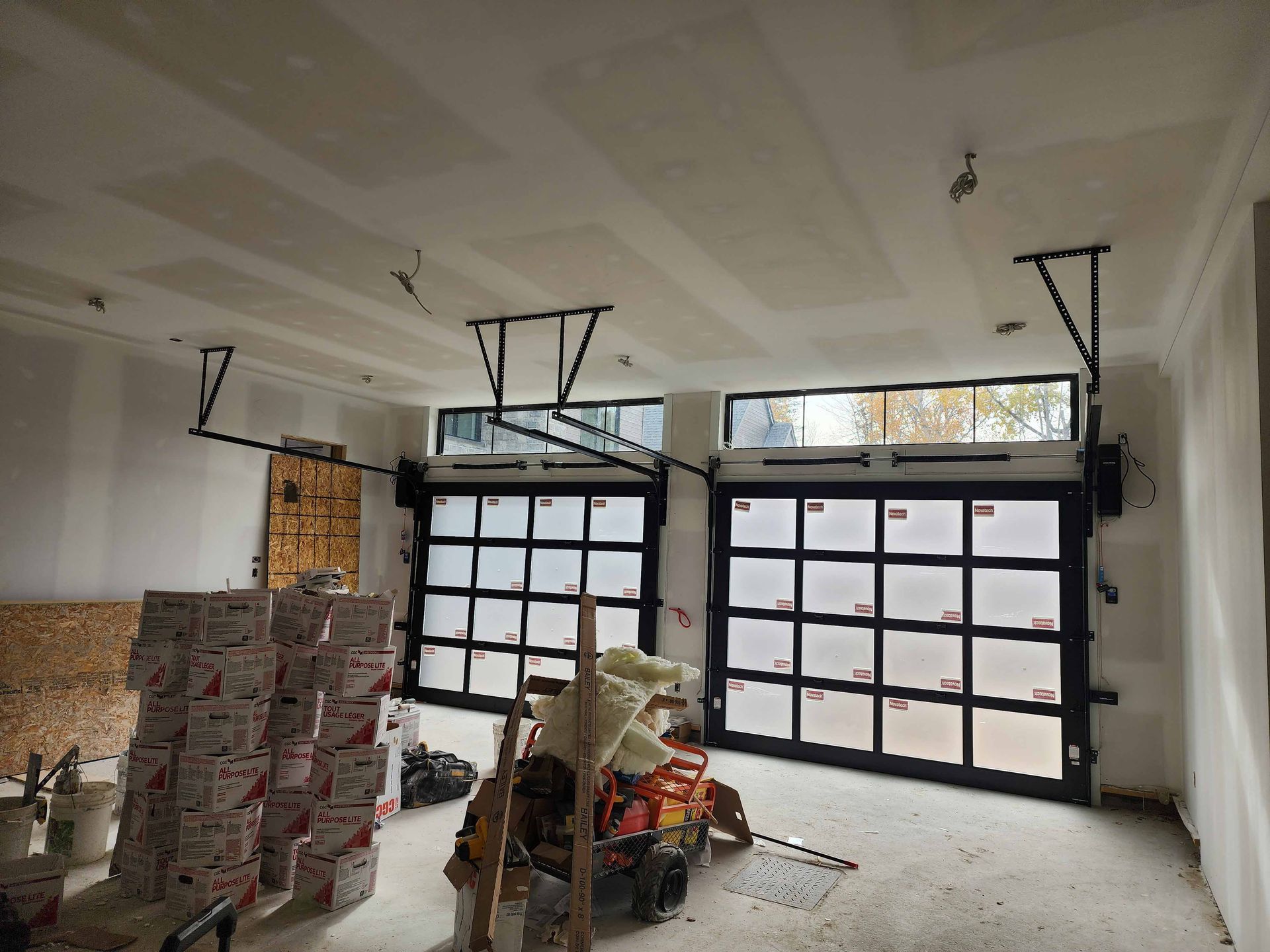 Un garage en construction avec deux portes de garage et des boîtes empilées sur le sol.