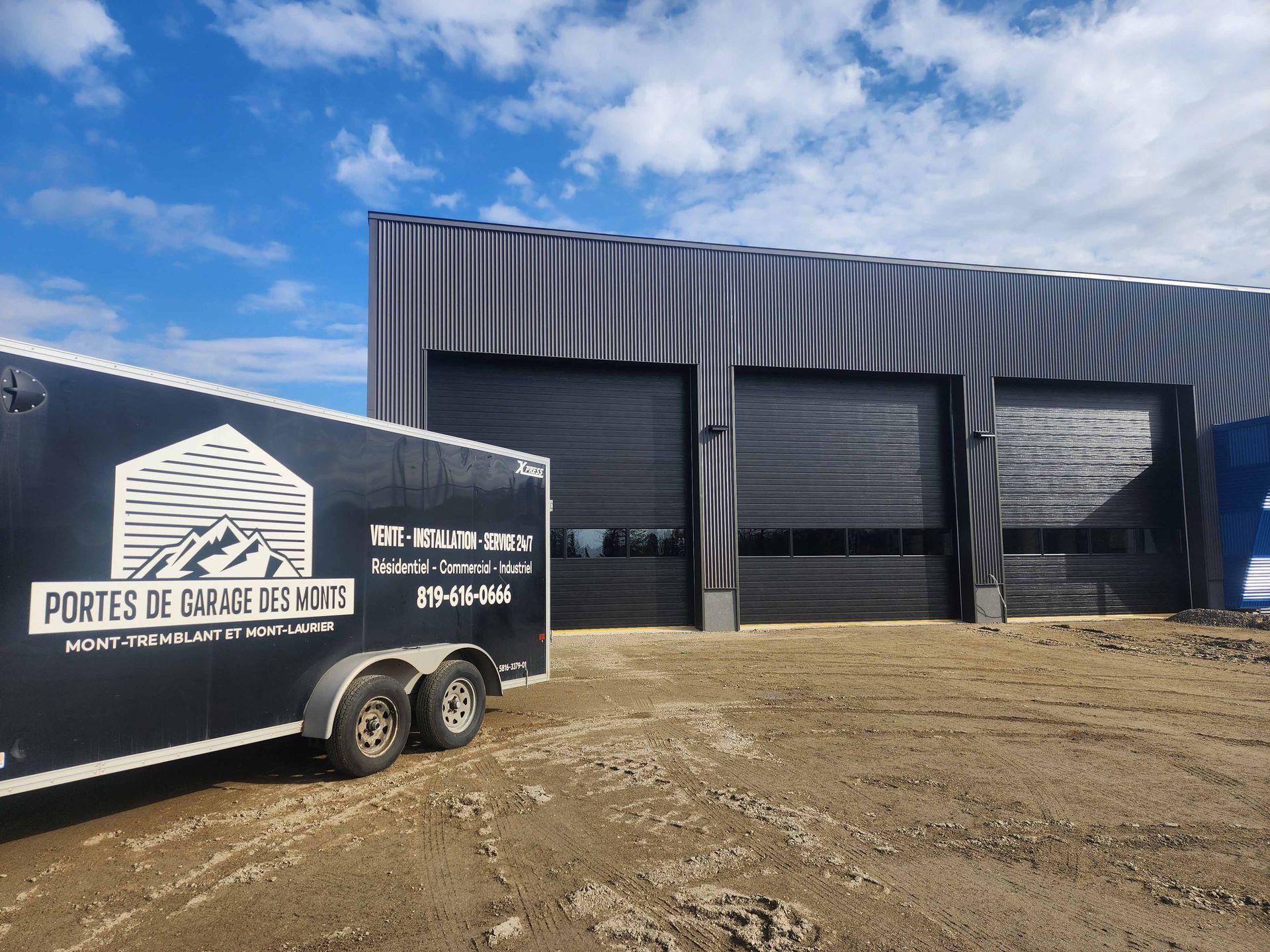 Portes de garage noires sur un bâtiment moderne ; remorque avec logo d'entreprise au premier plan.