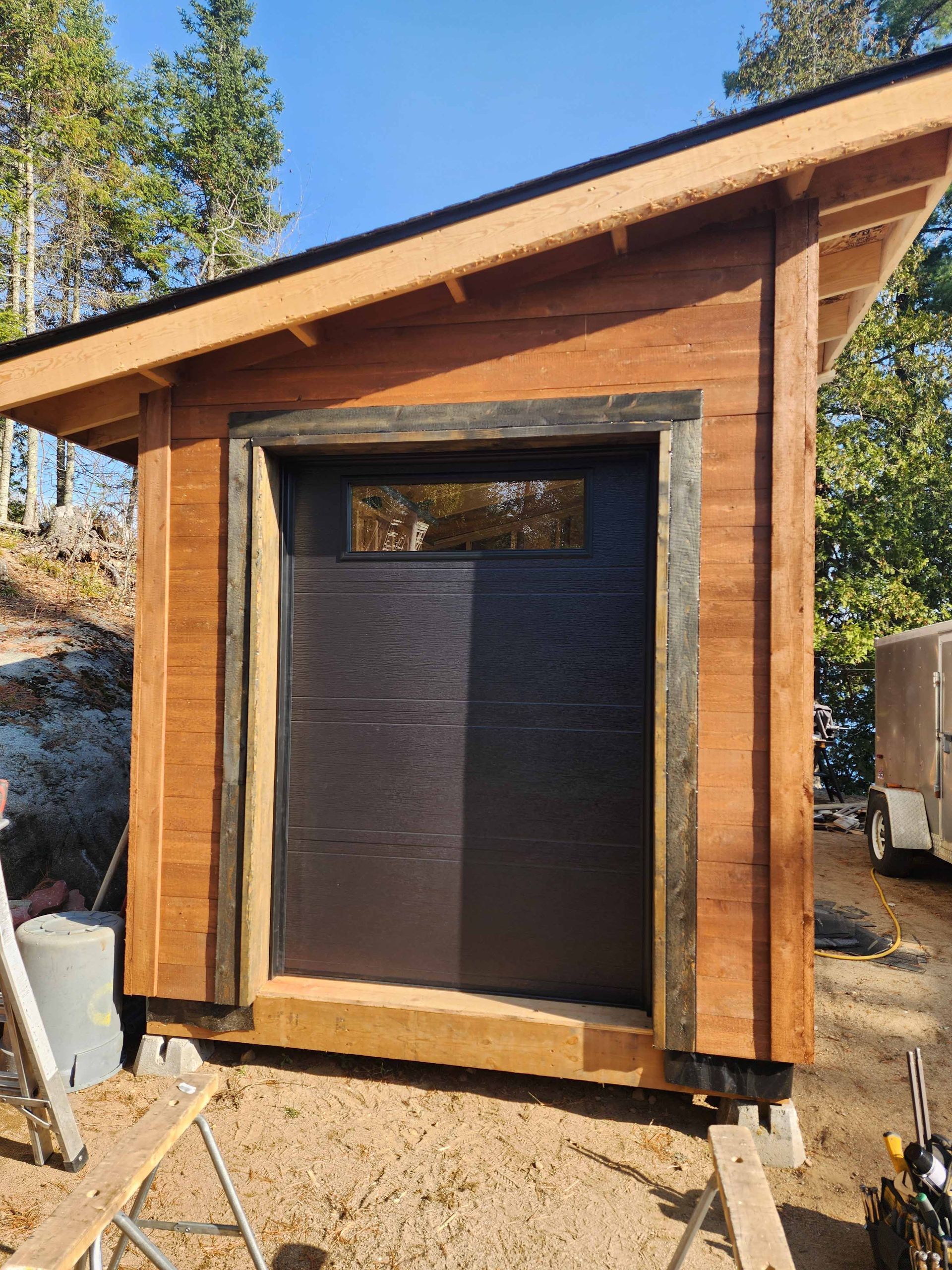 Un hangar en bois avec une porte de garage noire et une fenêtre.