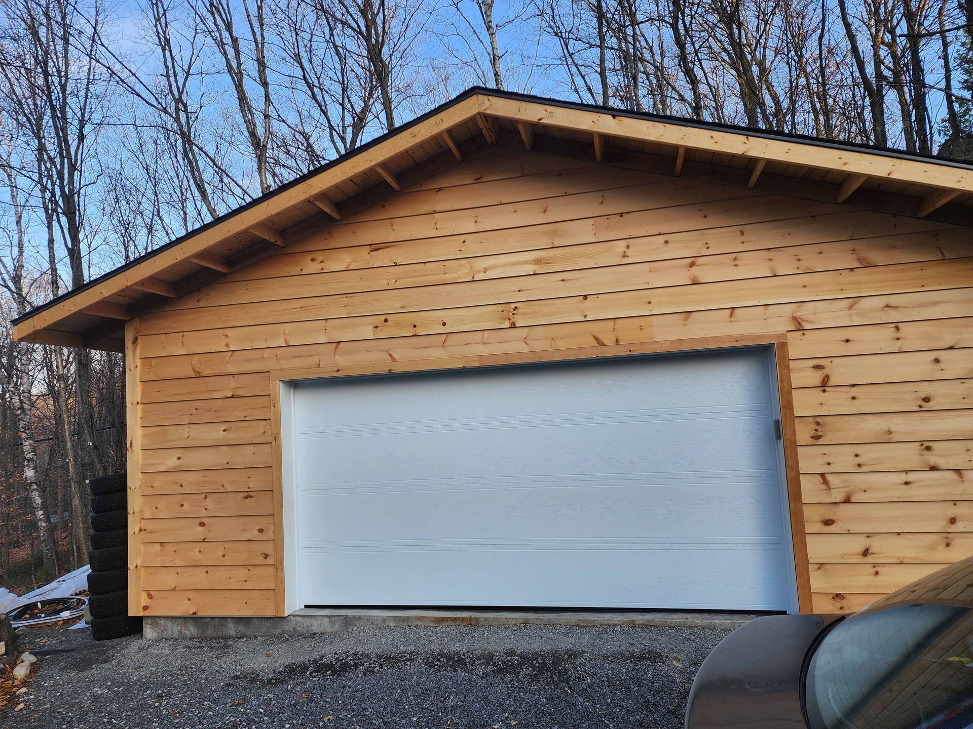 Une voiture est garée devant un garage en bois avec une porte de garage blanche.