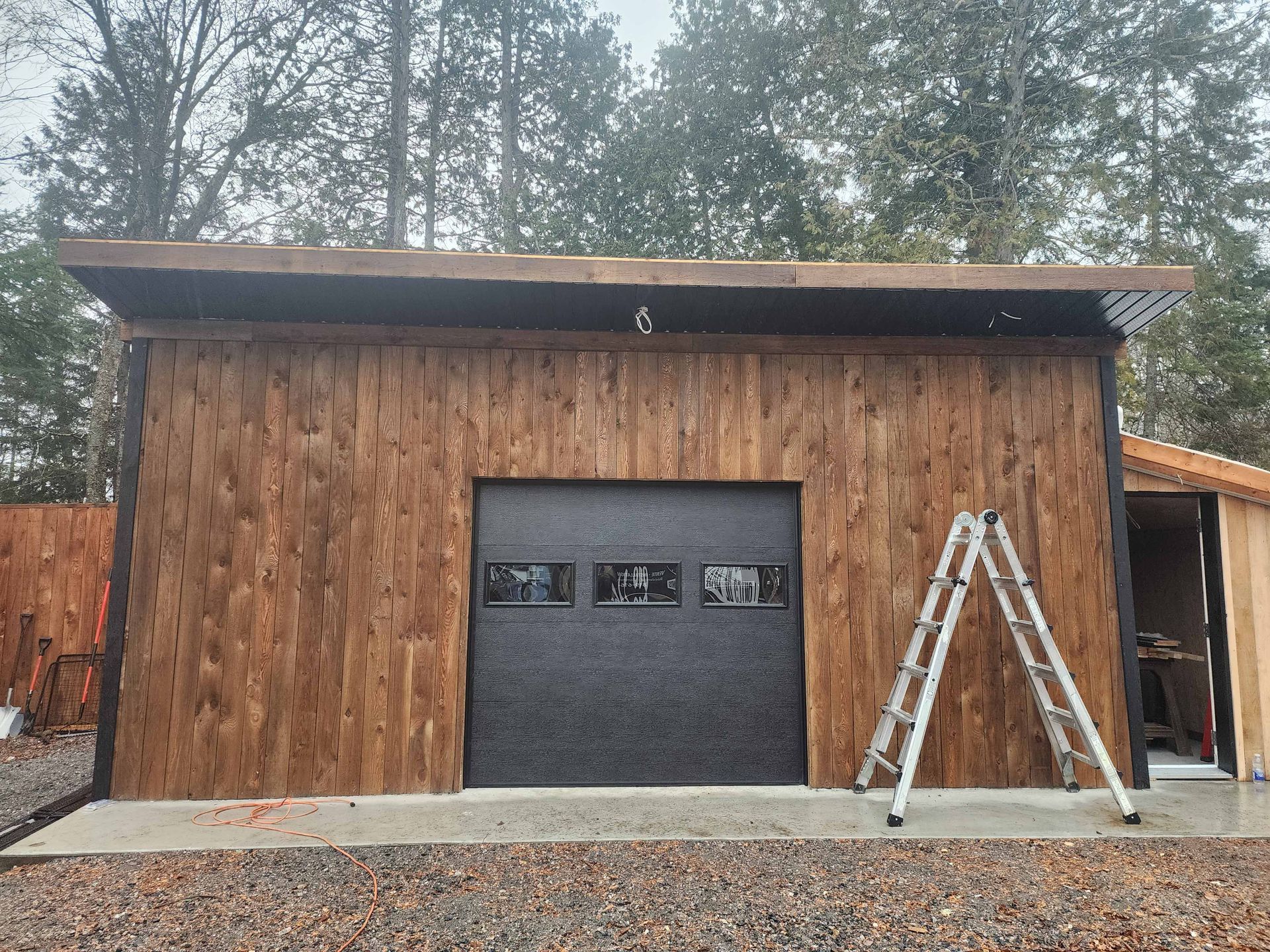 Un garage en bois avec une porte de garage noire et une échelle devant.