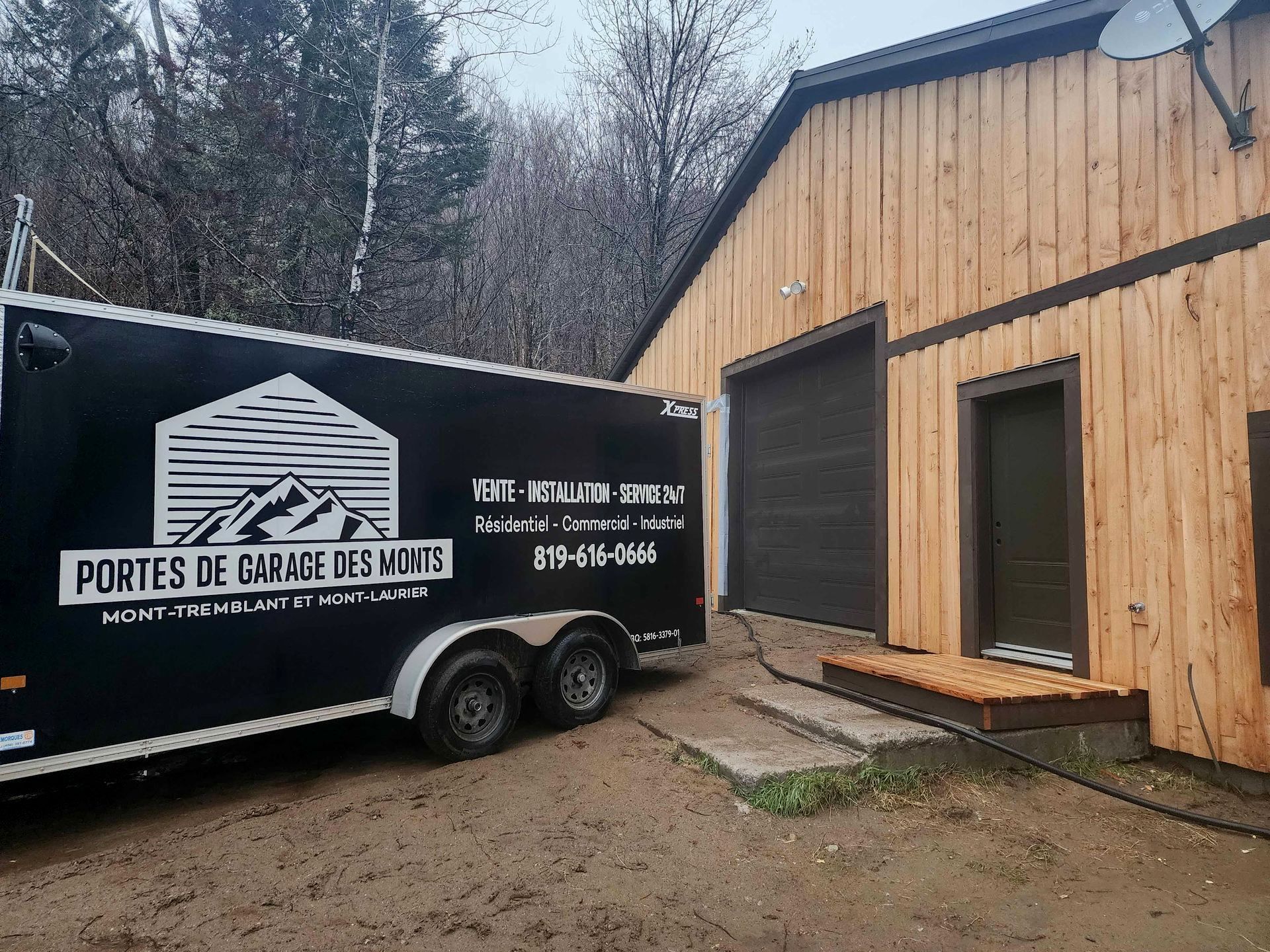 Une remorque noire est garée devant un bâtiment en bois.