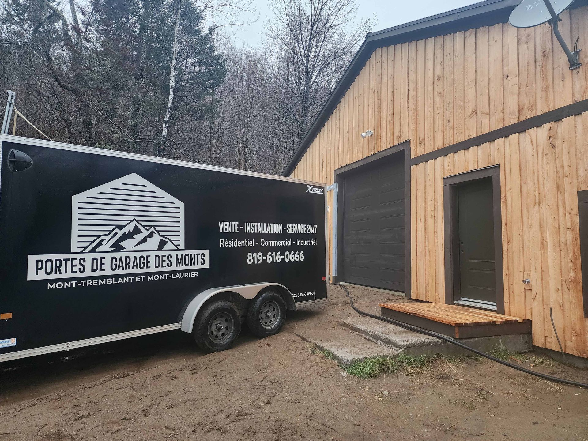 Une remorque noire est garée devant un bâtiment en bois.