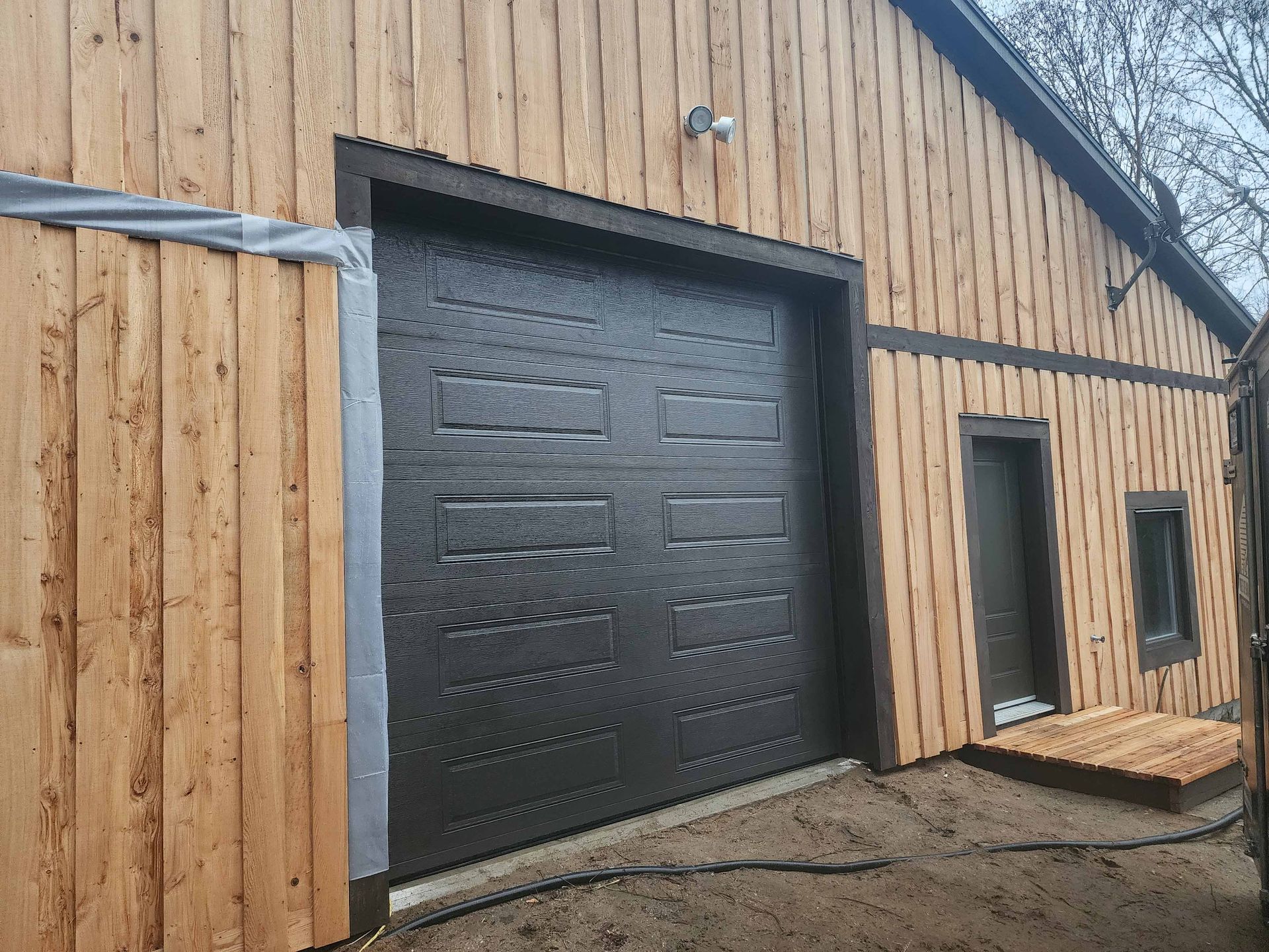 Porte de garage marron sur un bâtiment en bois, petite porte et fenêtre sur le côté, passerelle en bois.