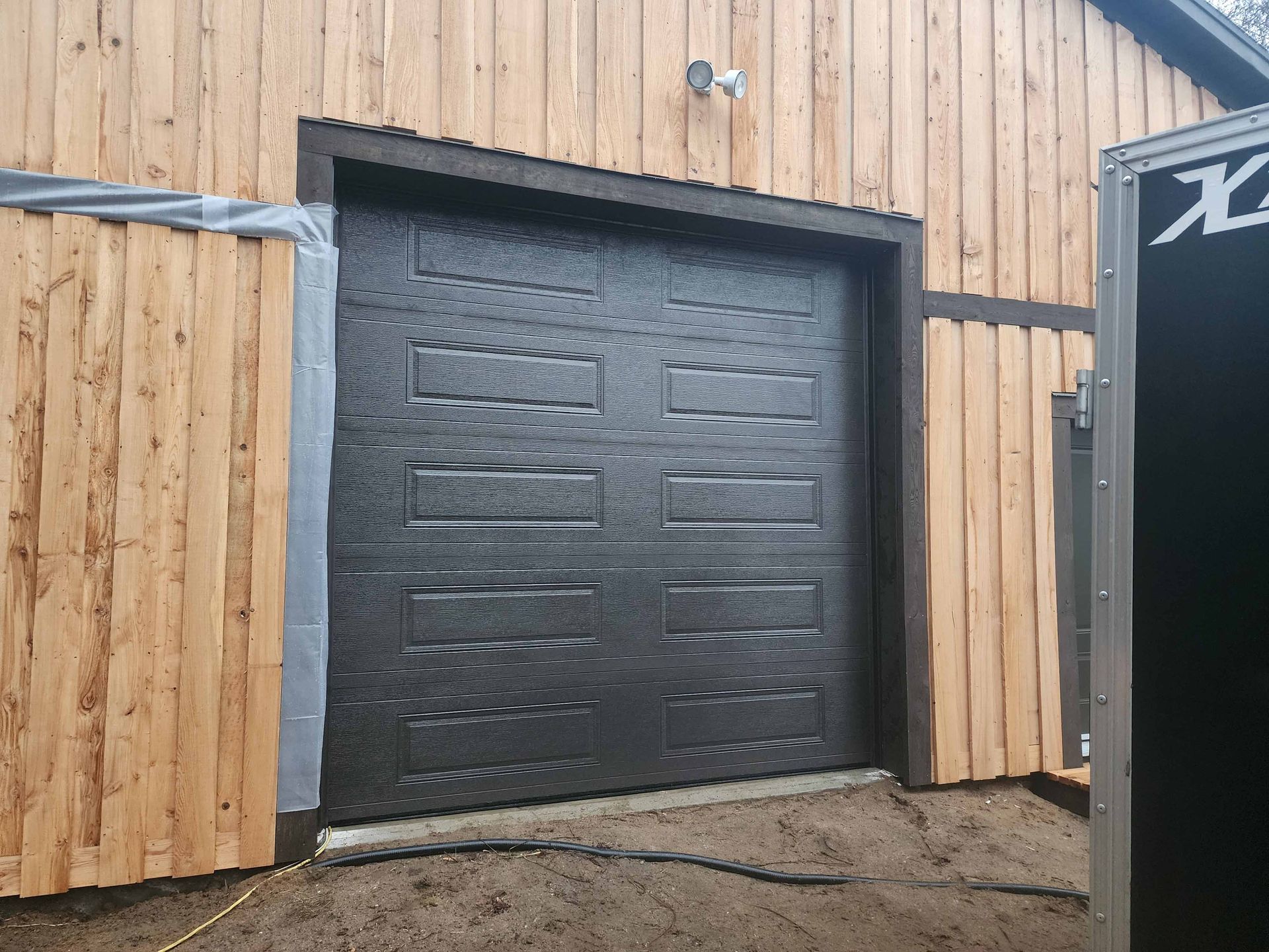 Une porte de garage noire se trouve devant un bâtiment en bois.