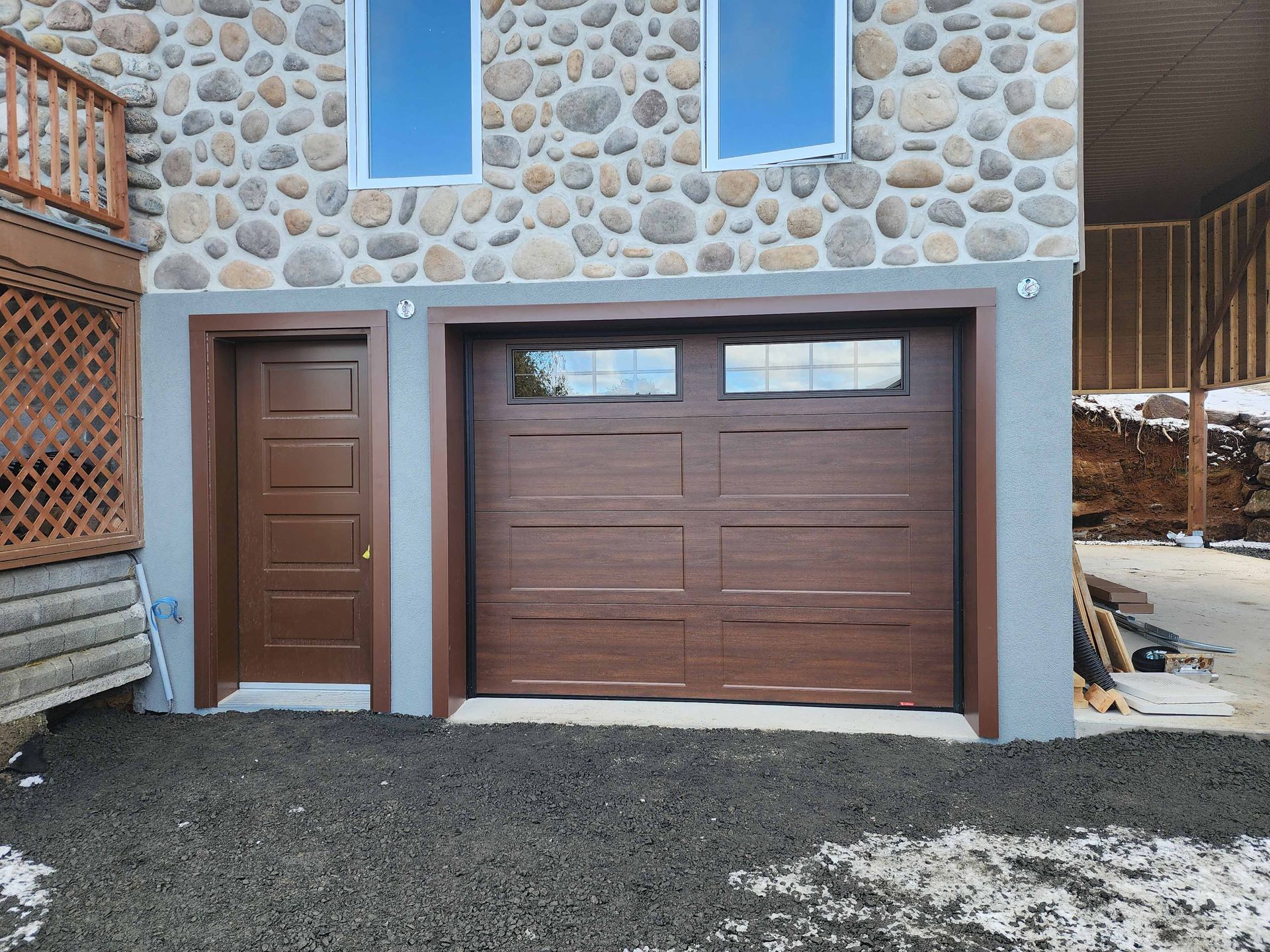 Porte de garage marron et porte sur une maison en pierre avec deux fenêtres au-dessus.