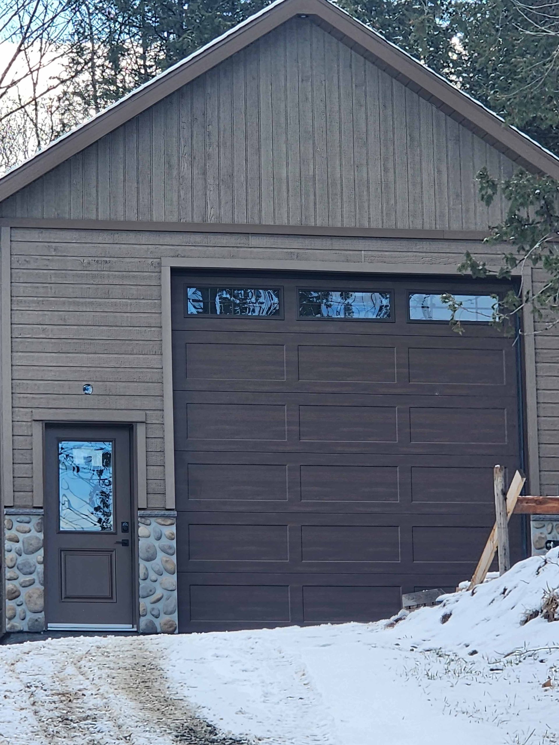 Garage brun avec porte assortie, base en pierre et neige.