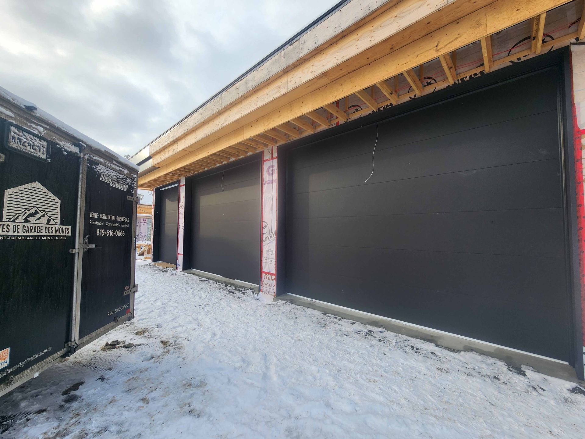 Une porte de garage est en cours de construction dans la neige à côté d'une remorque.