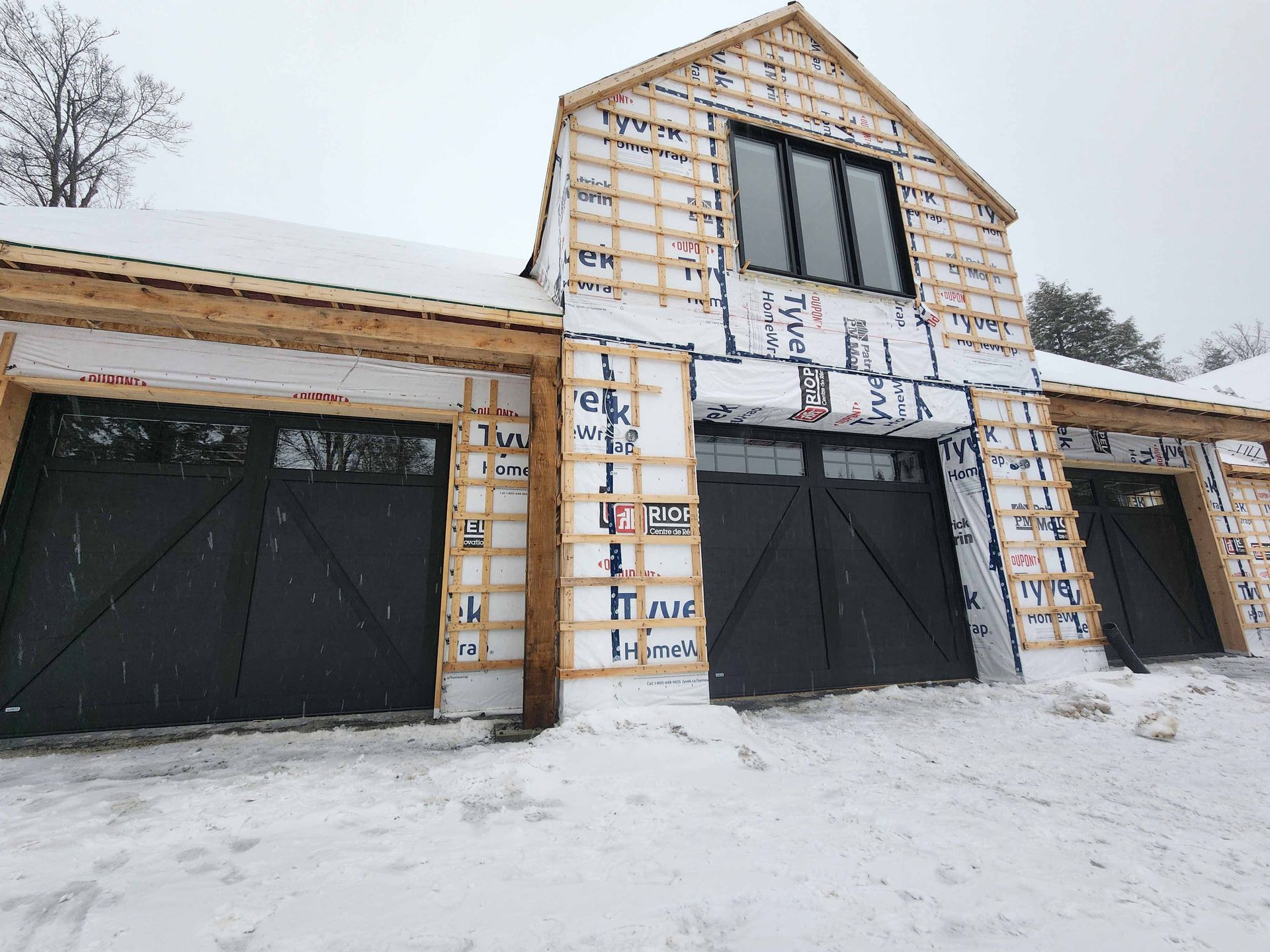 Trois portes de garage brun foncé ornées de motifs en X, encastrées dans un mur en béton, le sol étant enneigé.