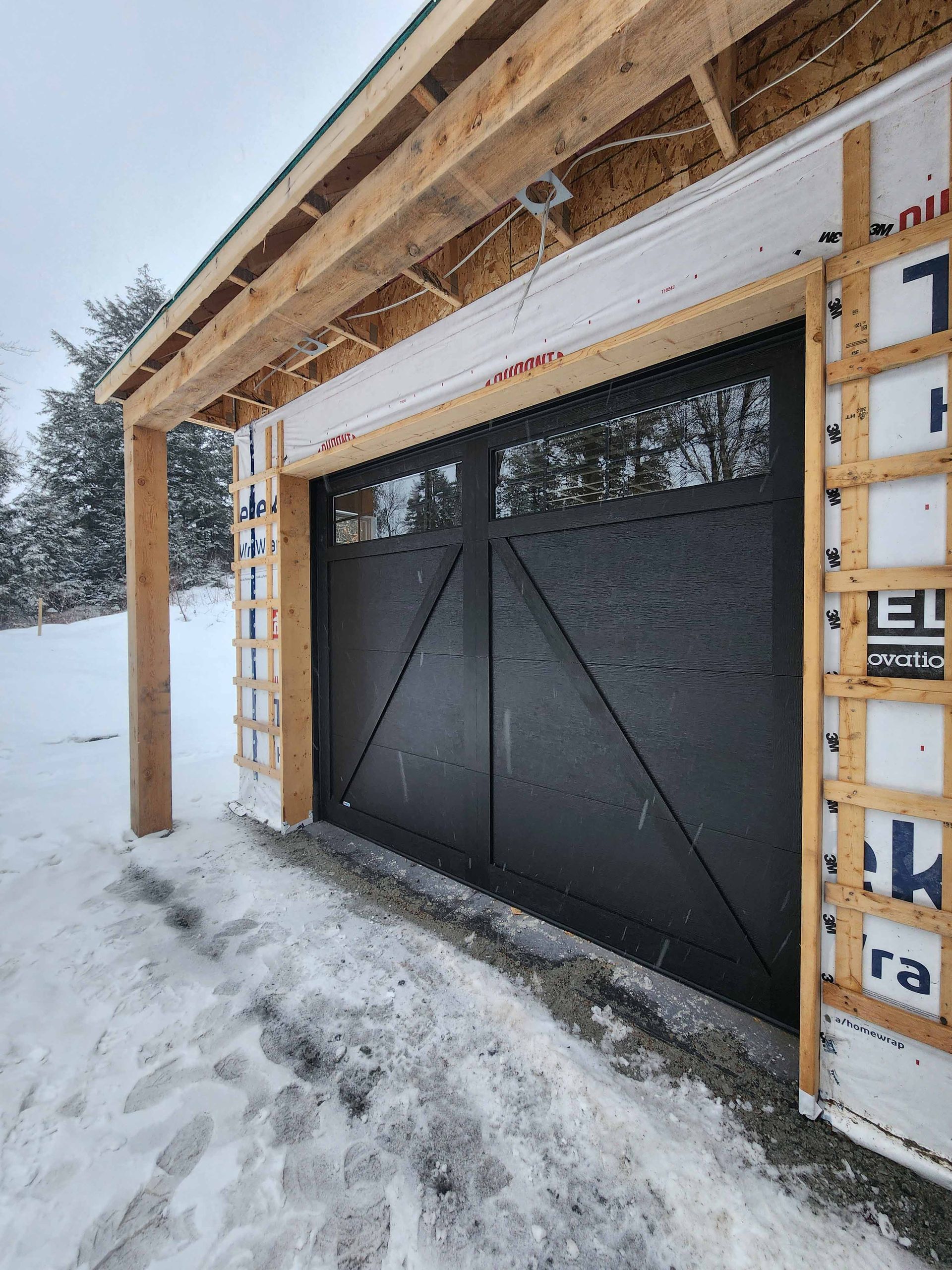 Une porte de garage noire est en cours de construction dans la neige.