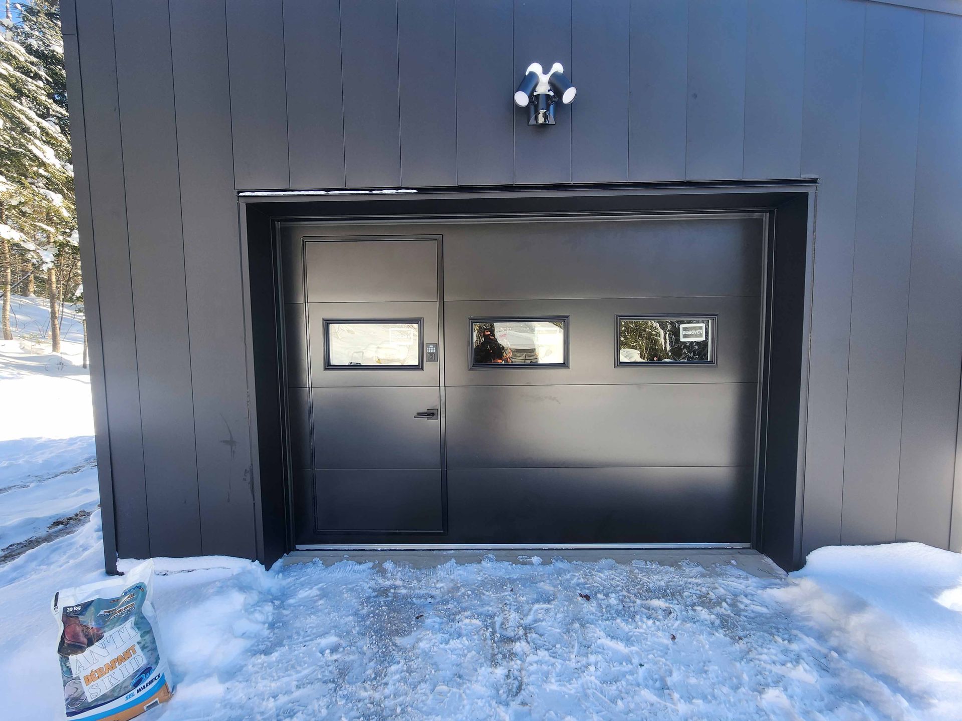 Une porte de garage noire est posée dans la neige à côté d'un sac de neige.