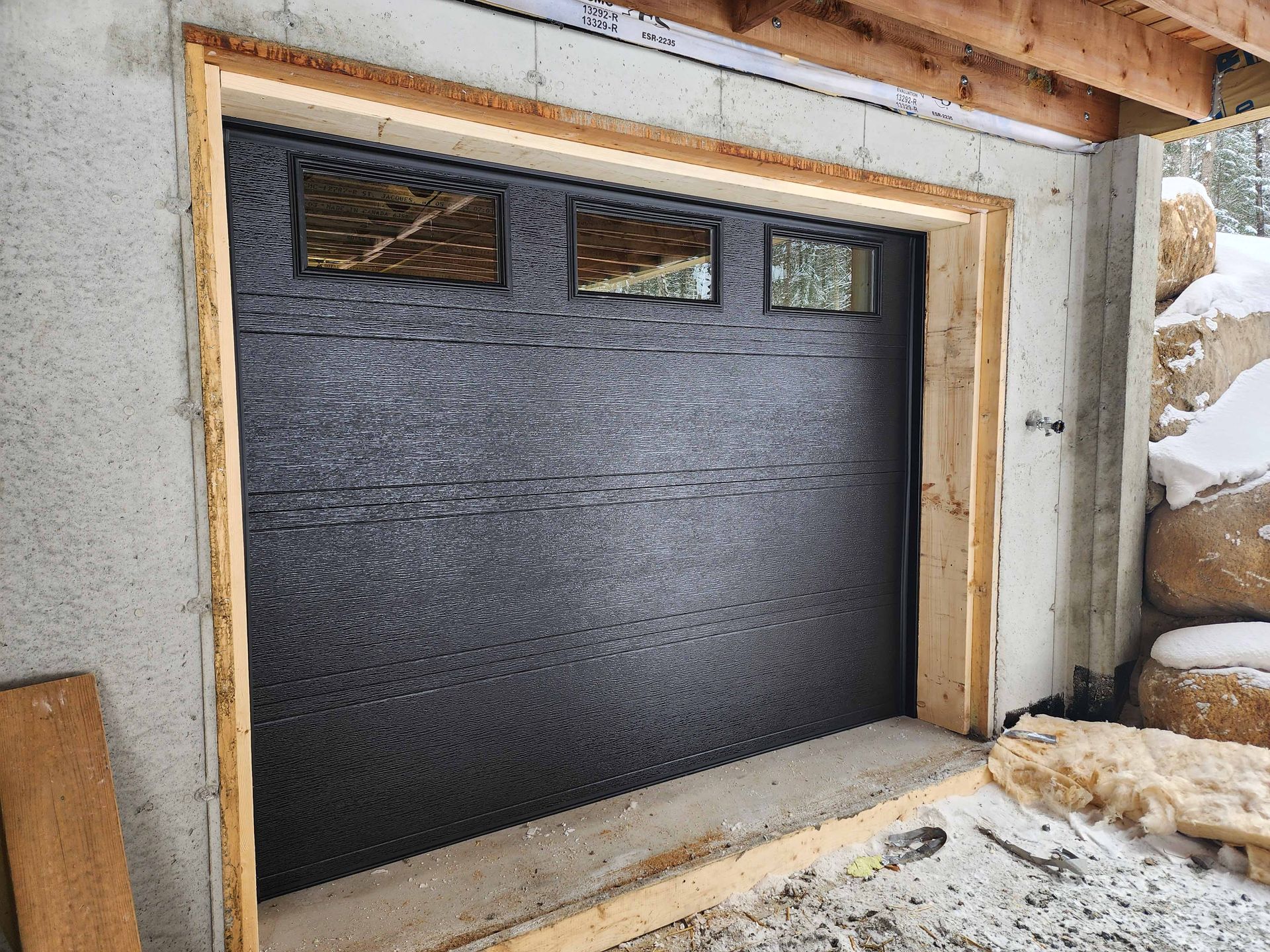 Une porte de garage noire est en cours d'installation dans un garage en béton.