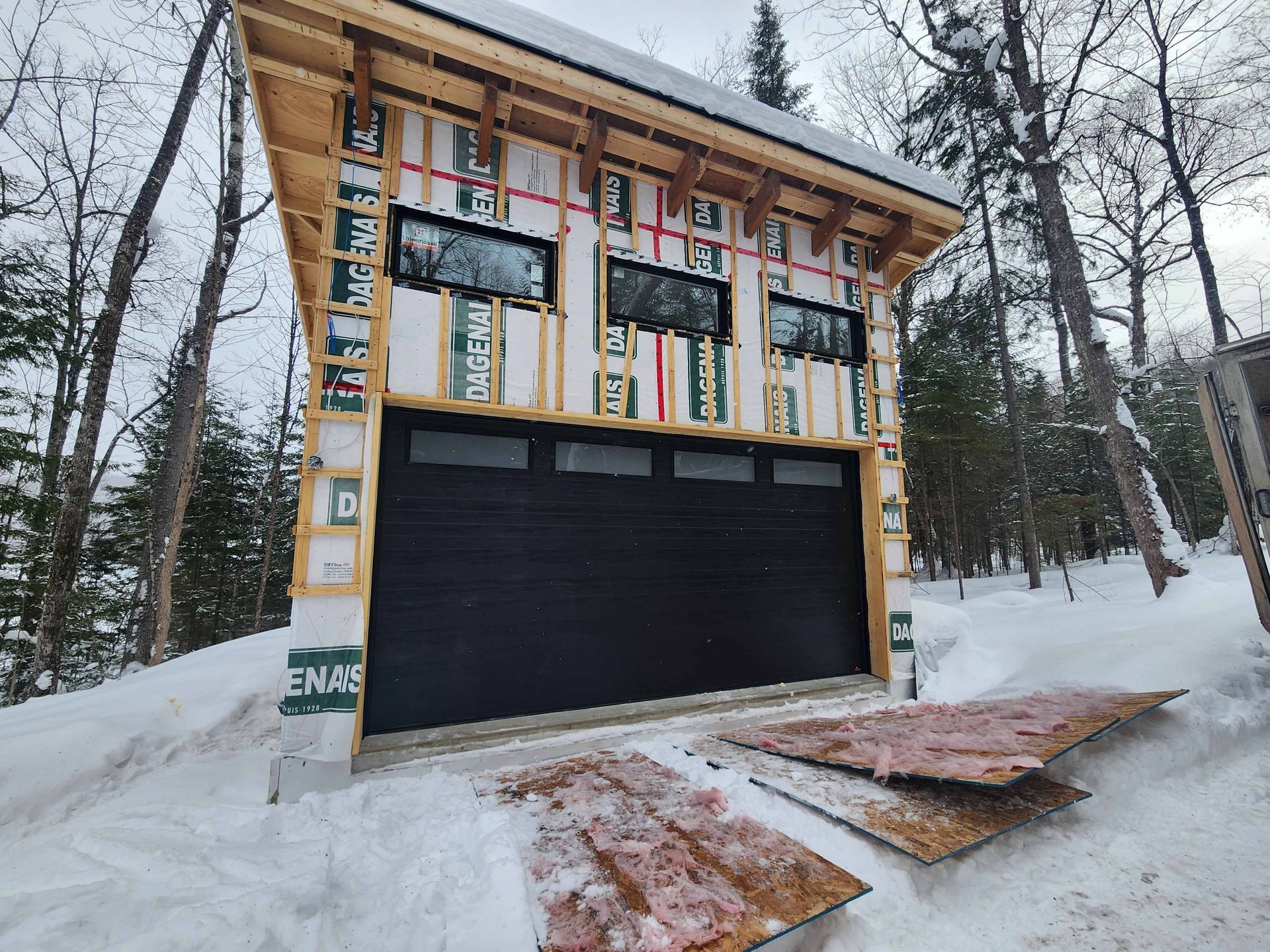 Un garage est en cours de construction dans la neige avec une porte de garage noire.