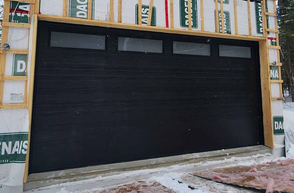 Une porte de garage noire est entourée d'une rangée de feuilles de béton