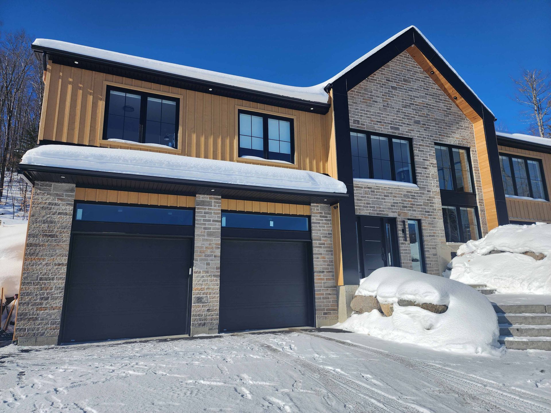 Une grande maison avec deux portes de garage est recouverte de neige.