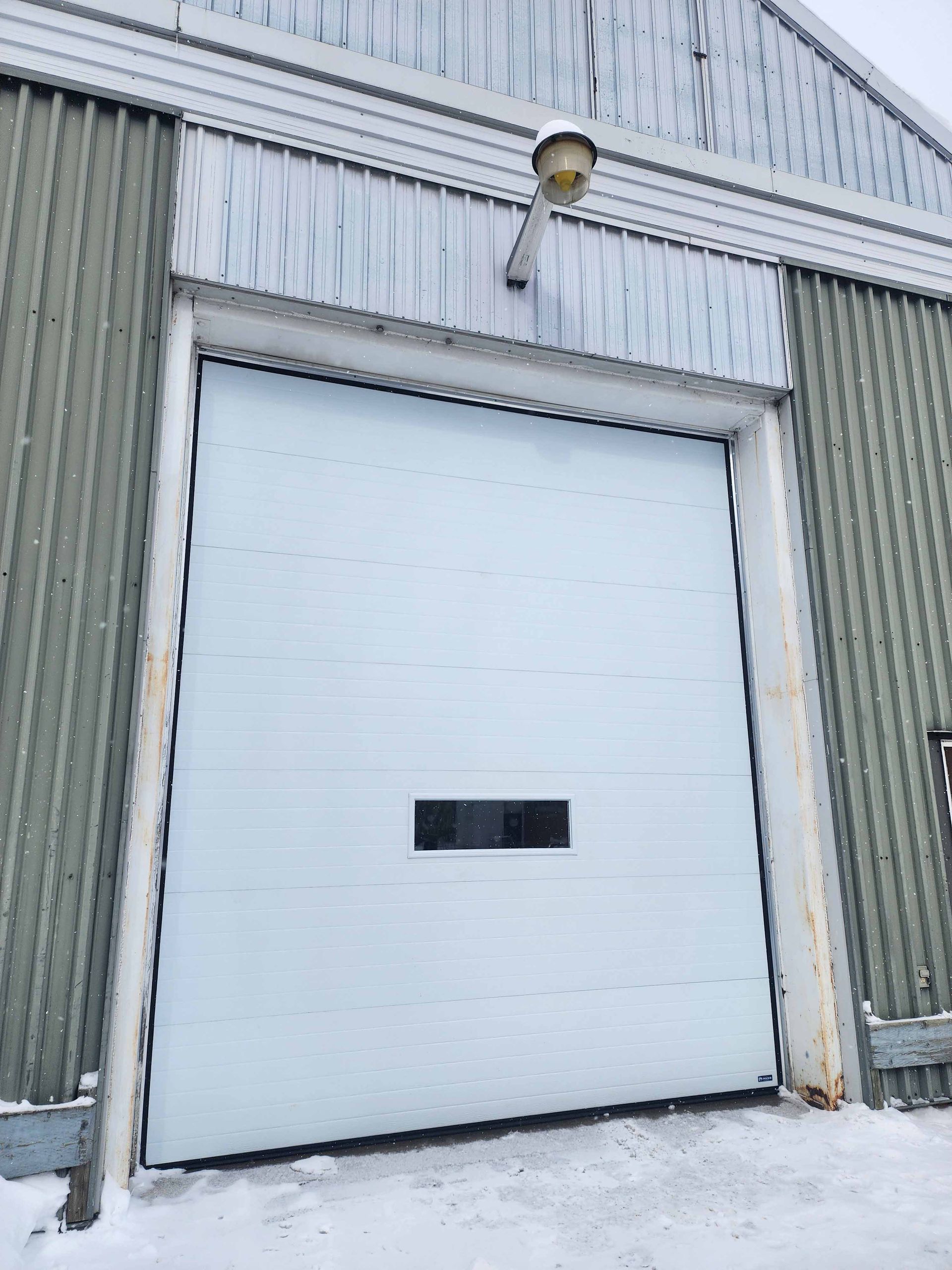 Une porte de garage blanche est ouverte un jour de neige