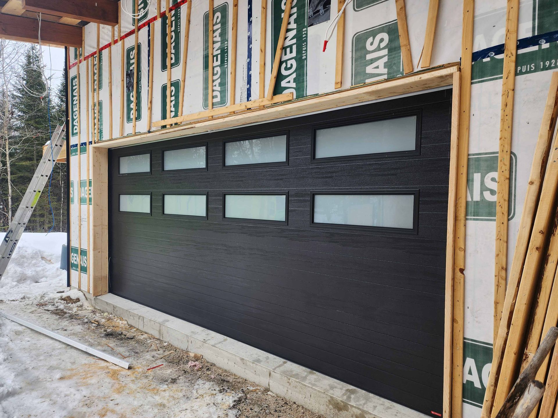 Une porte de garage est en cours d'installation sur le côté d'une maison en construction.