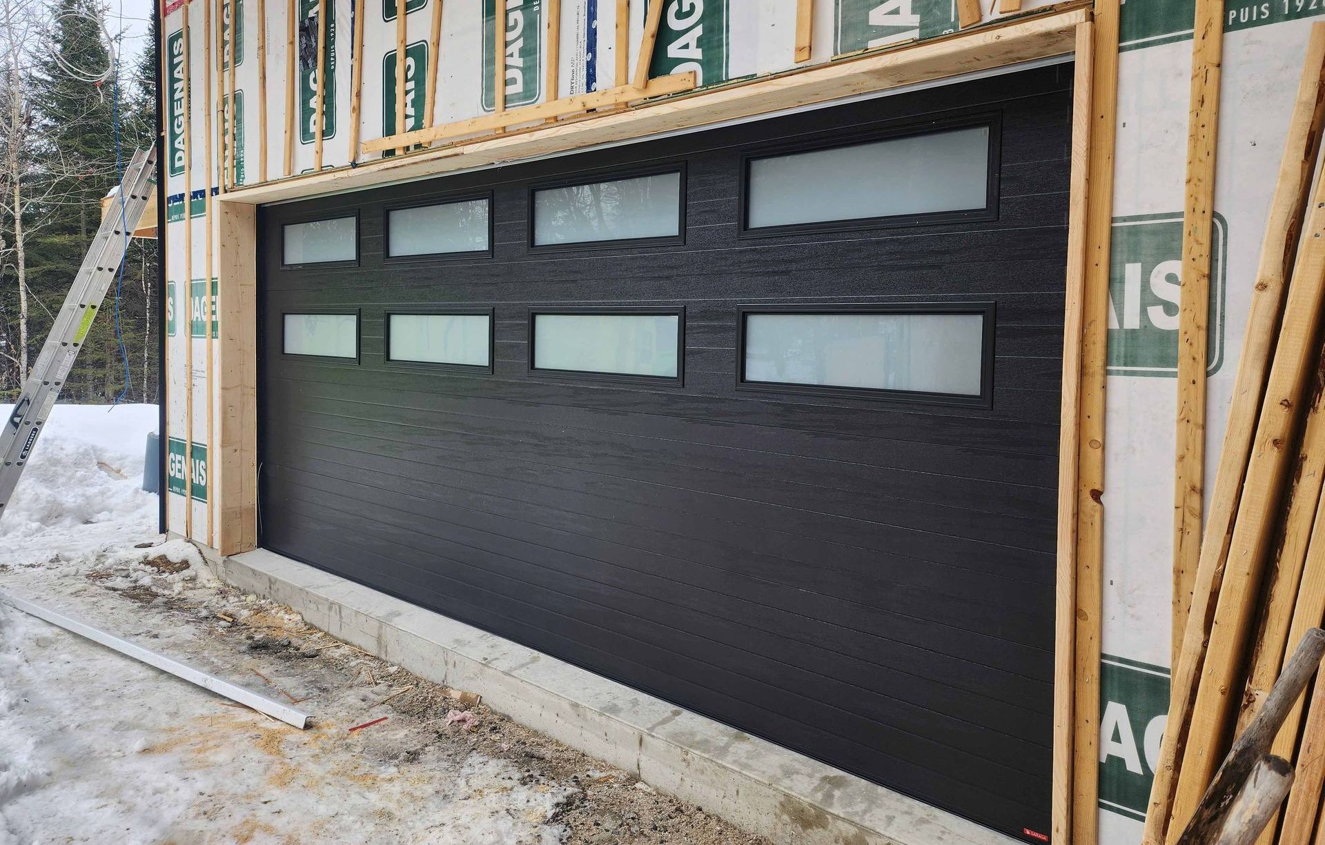 Une porte de garage noire est en cours d'installation sur une maison en construction.