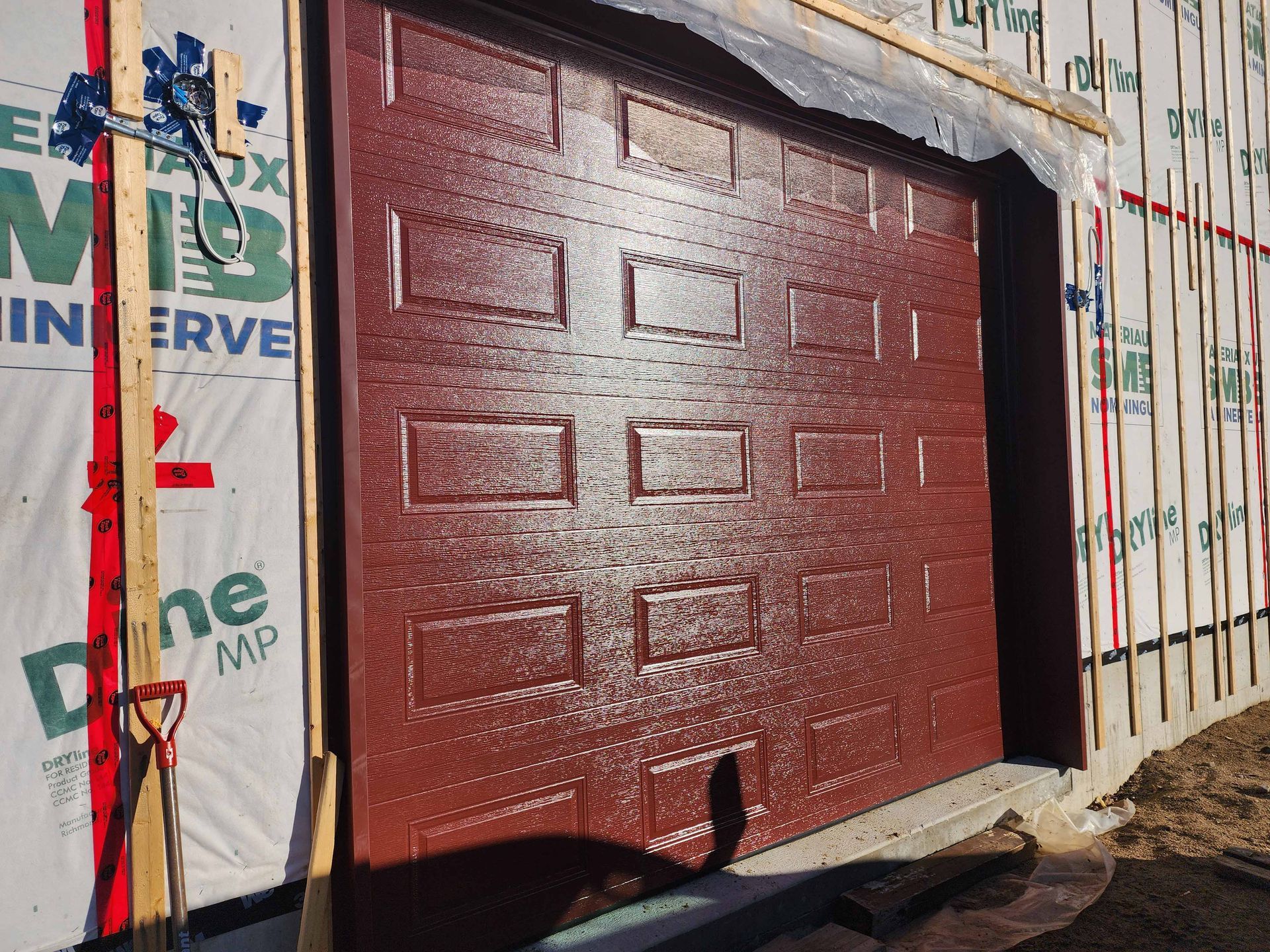Une porte de garage rouge est en cours d'installation sur une maison