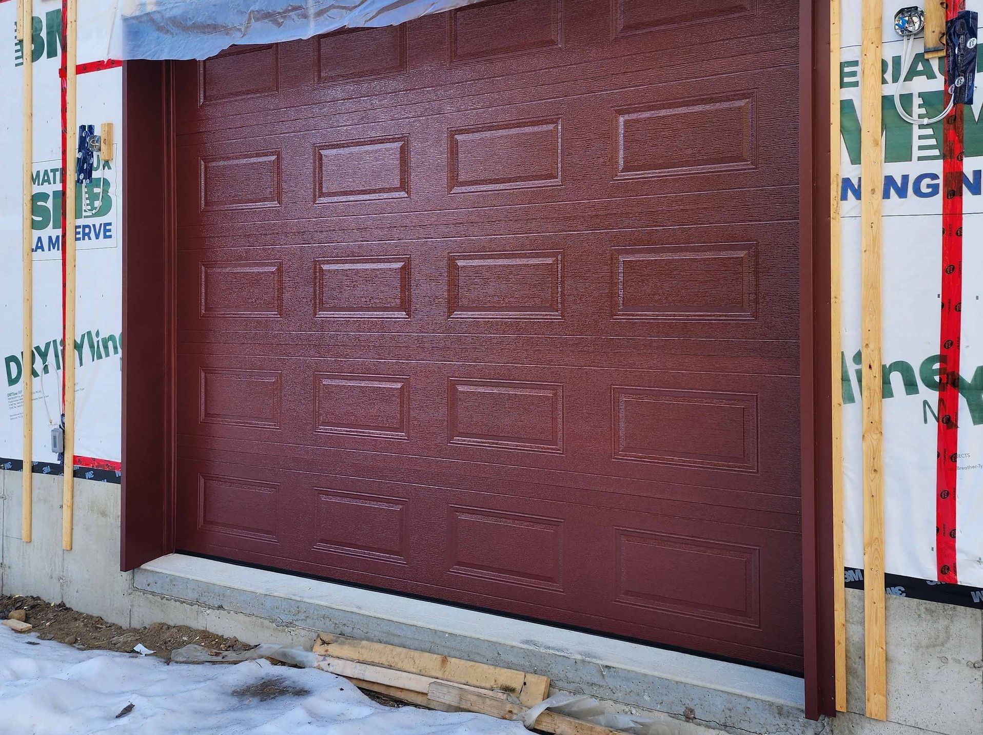 Une porte de garage rouge est en cours d'installation sur le côté d'une maison.