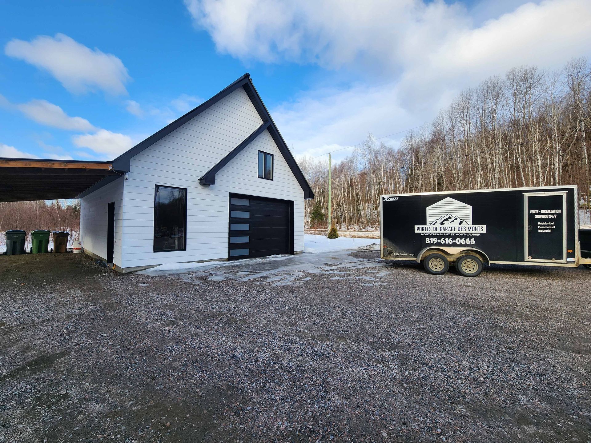 Une maison blanche avec une caravane noire garée devant.