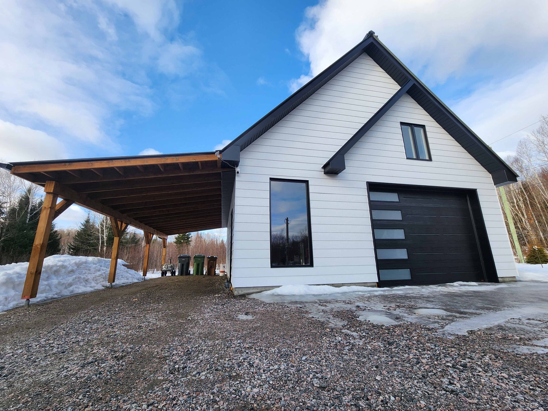 Une maison blanche avec une porte de garage noire et un abri voiture.