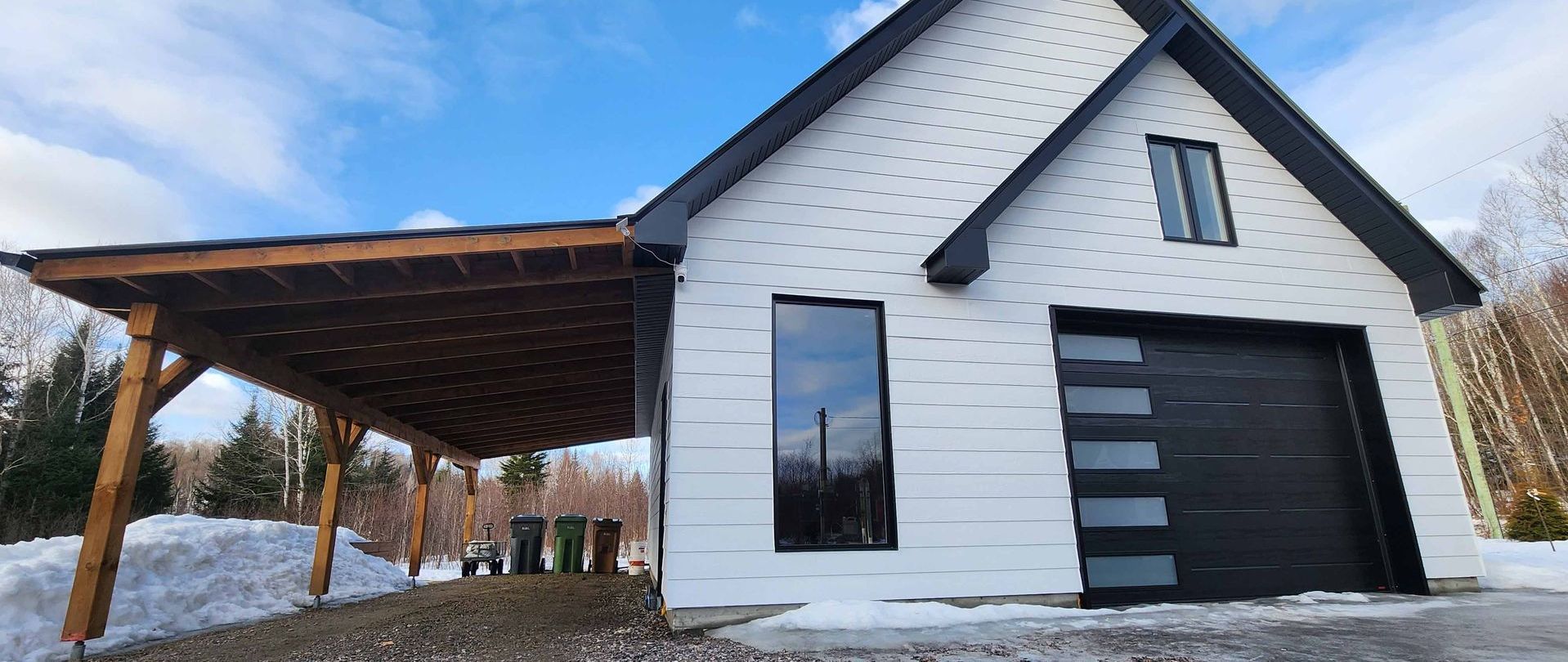 Une maison blanche avec une porte de garage noire et un abri voiture.