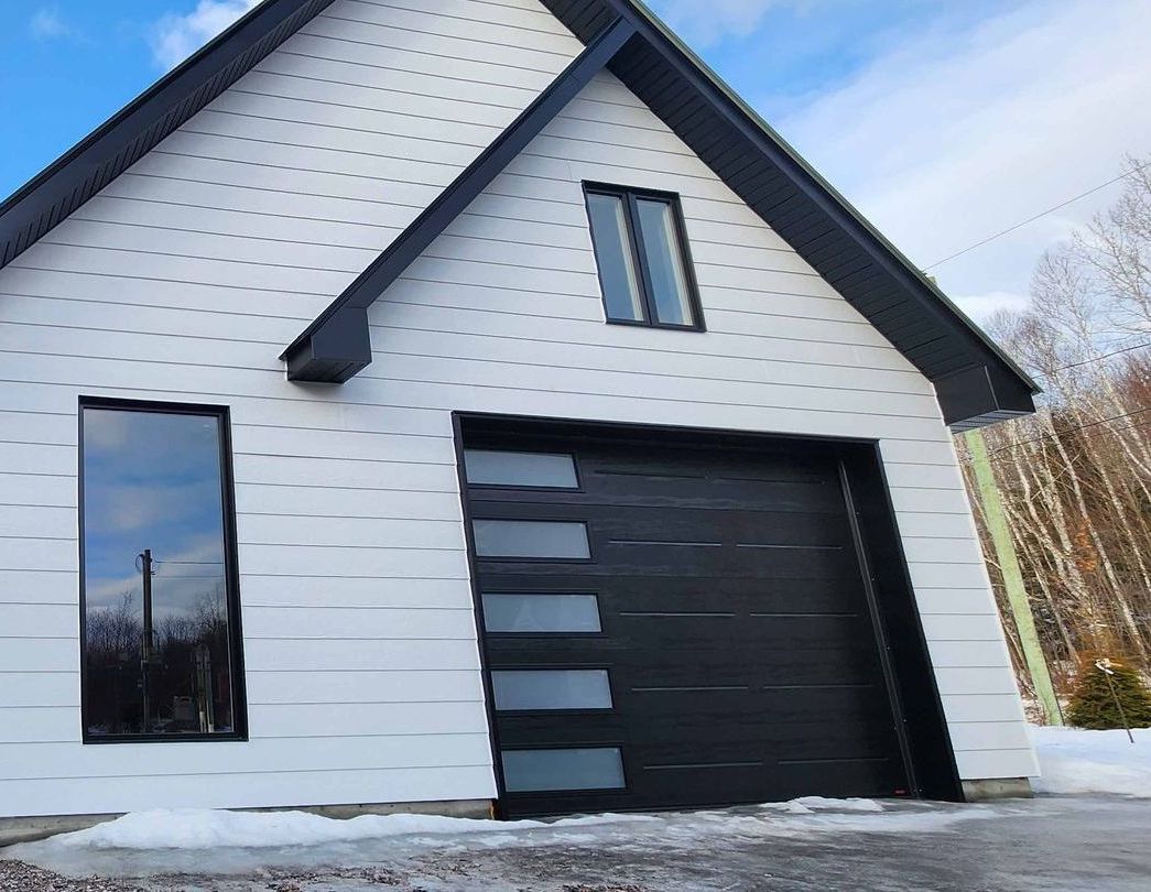 Porte de garage noire avec panneaux de verre sur une maison blanche avec garniture noire.