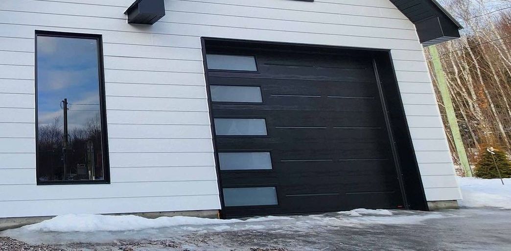 Une maison blanche avec une porte de garage noire et une fenêtre.