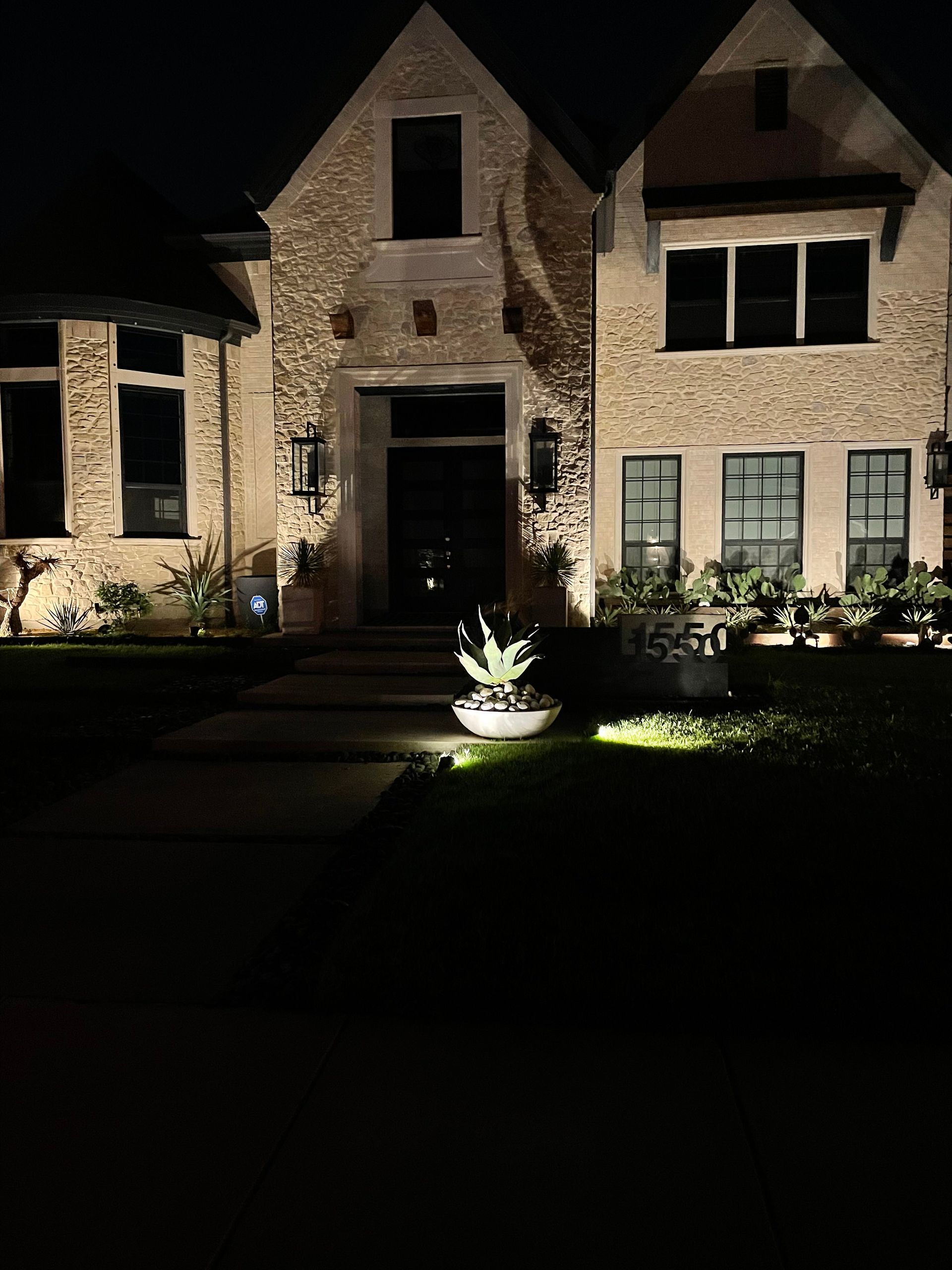 A large brick house is lit up at night with a potted plant in front of it.