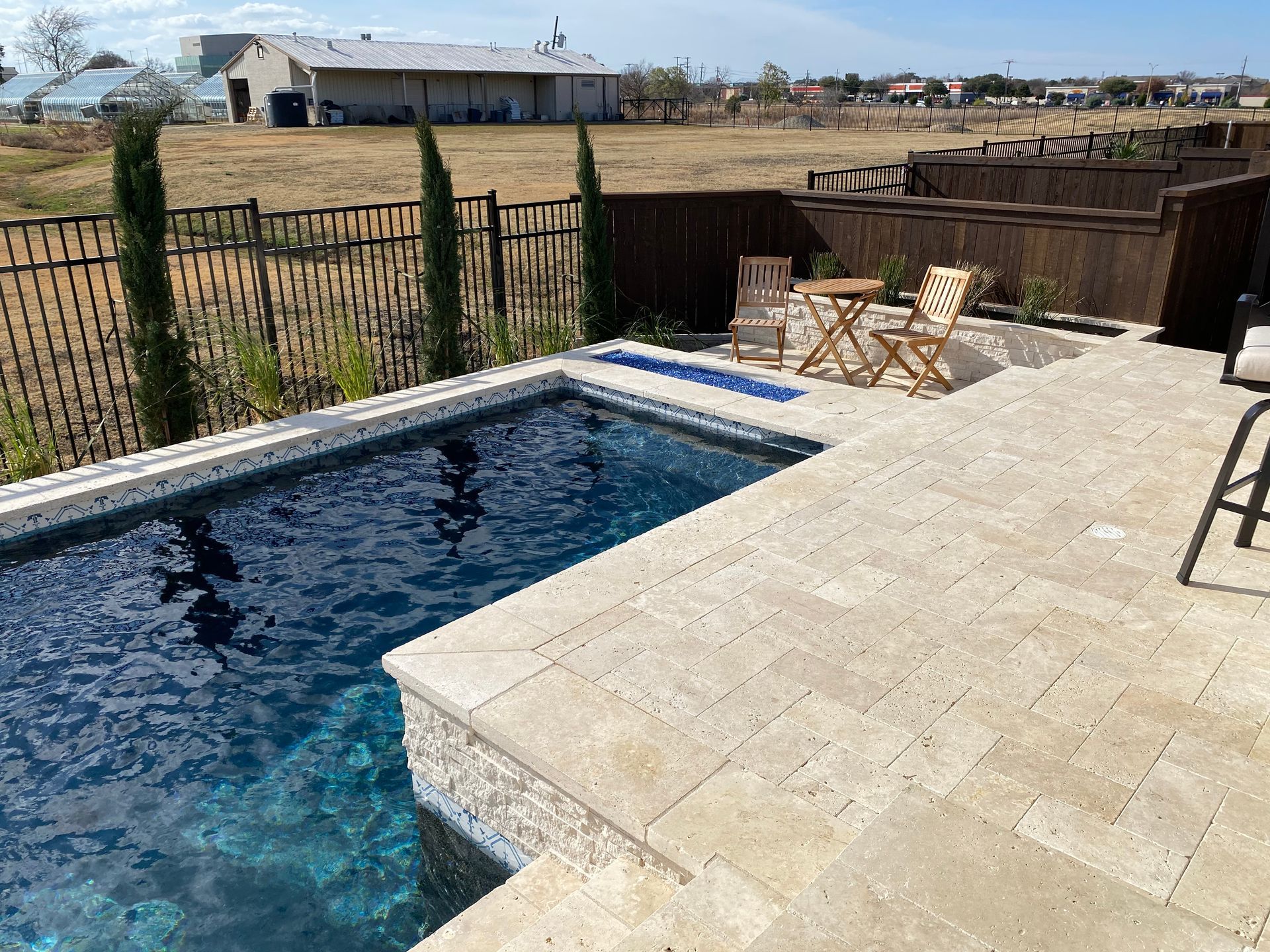 A large swimming pool is surrounded by a fence and chairs.