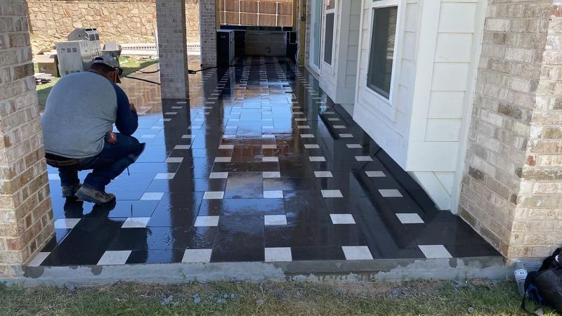 A man is kneeling on a tiled floor in front of a house.