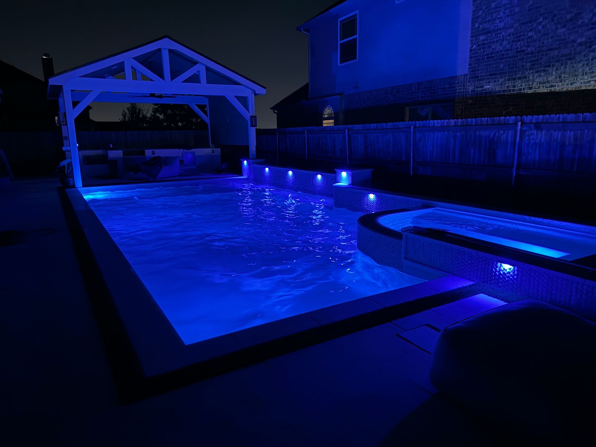 A large swimming pool is lit up at night with blue lights.