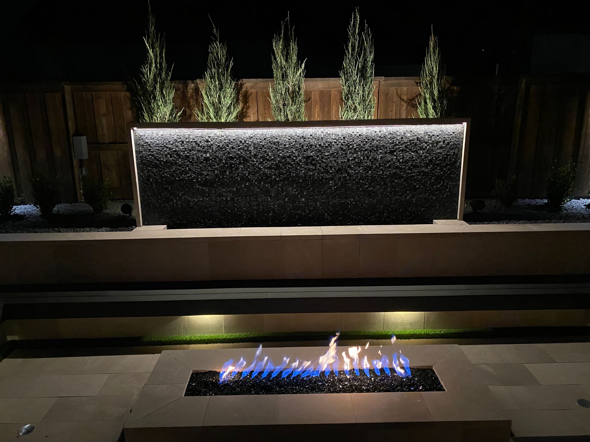 A fire pit with a waterfall in the background is lit up at night.