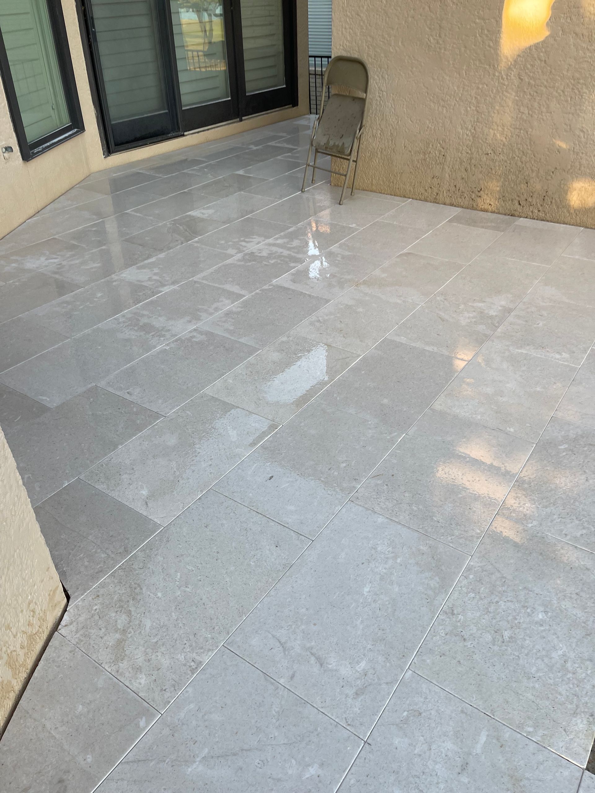 A tiled patio with a chair and sliding glass doors.
