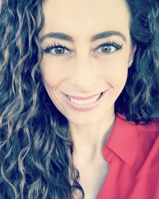 A woman with curly hair is smiling and wearing a red shirt.
