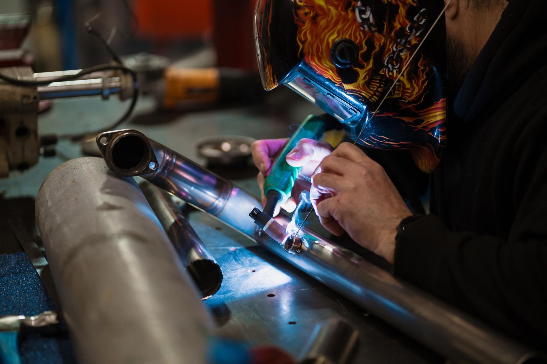 A man wearing a welding mask is welding a metal pipe.