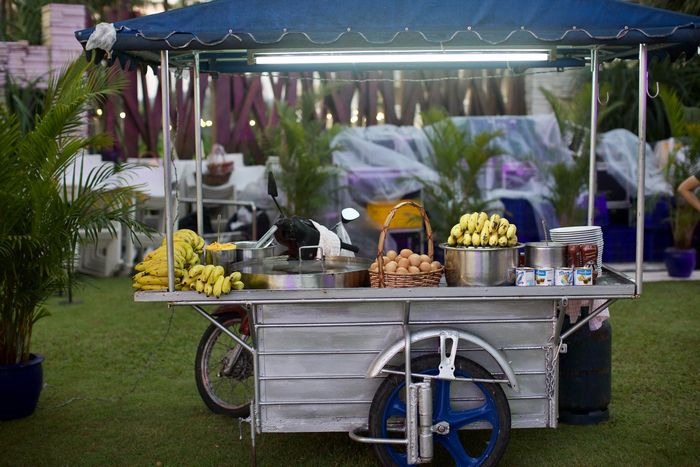 A food cart with bananas and eggs on it is parked in the grass.