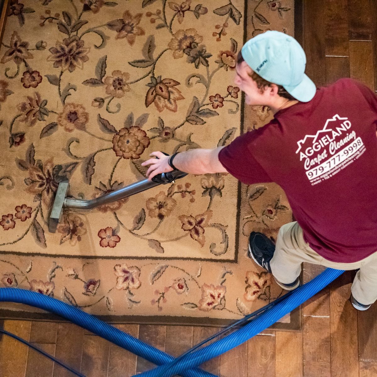 a man wearing a burgundy shirt that says aggieland carpet cleaning is vacuuming a rug