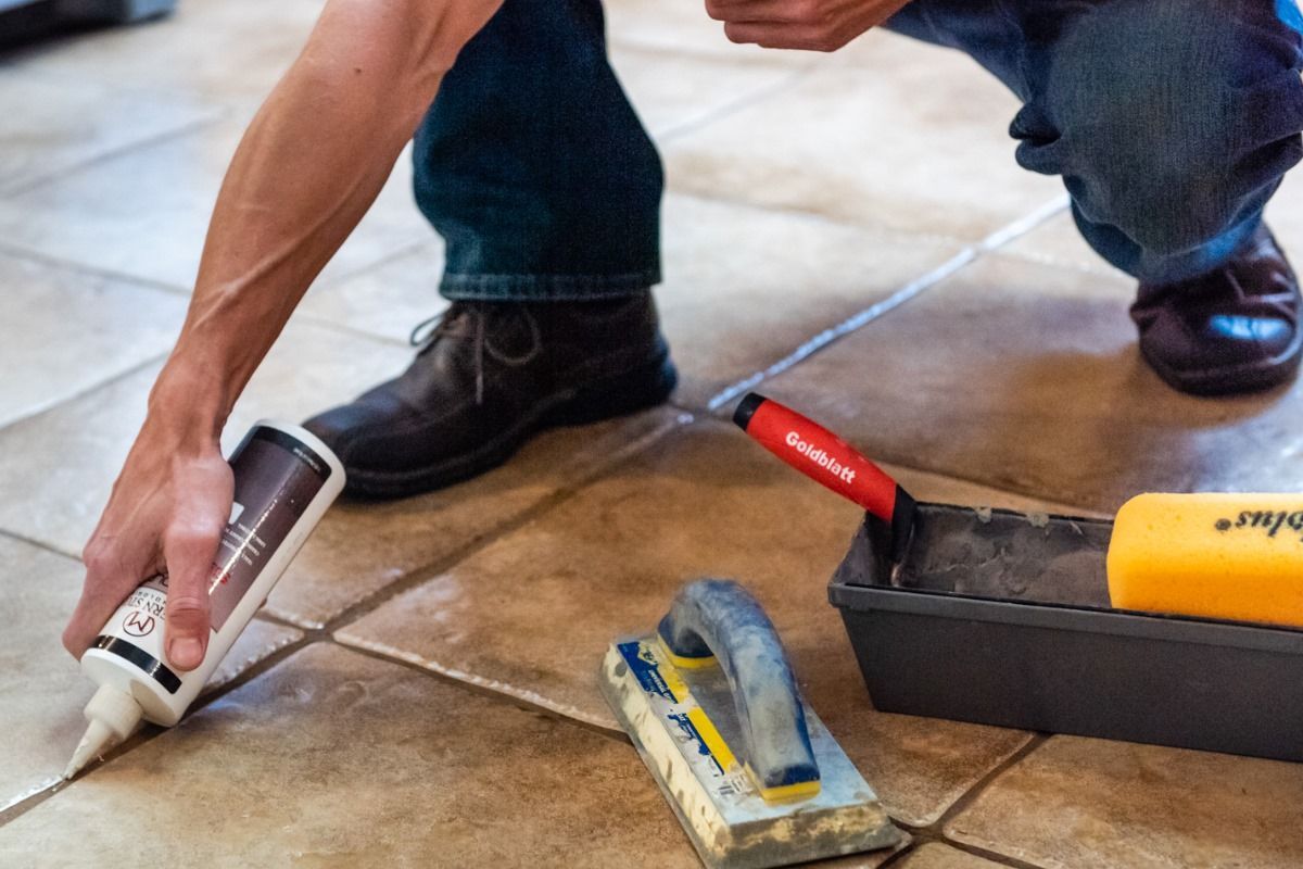 a man is kneeling down on a tiled floor holding a bottle of glue .